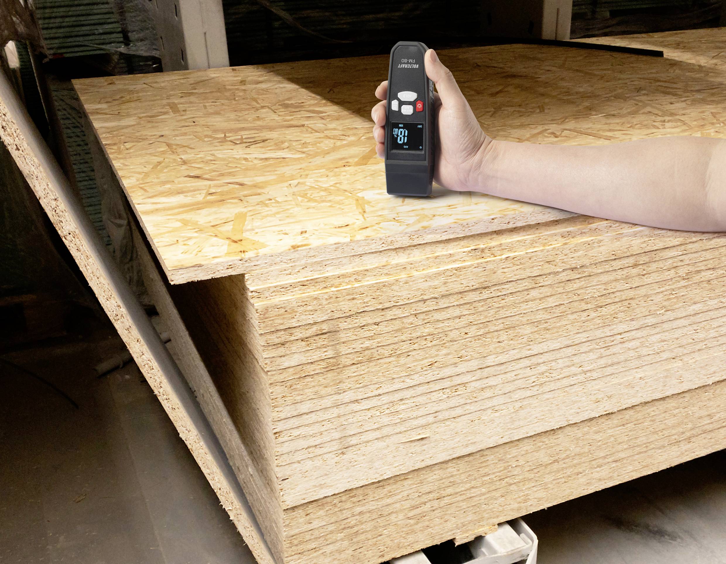 Eine Person misst mit einem digitalen Gerät die Dicke eines Stapels von Sperrholzplatten in einer Werkstattumgebung.