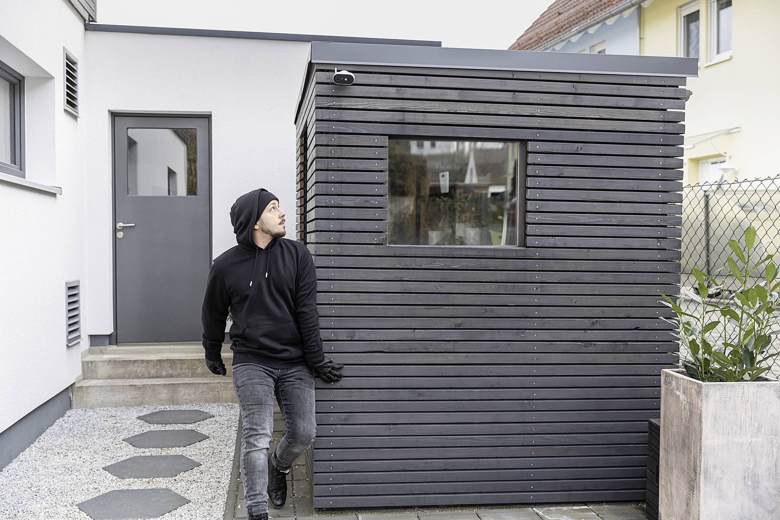 Person in dunkler Kleidung zieht ein modernes, kleines Gartenhaus über einen Kiesweg. Im Hintergrund ist ein helles Gebäude.