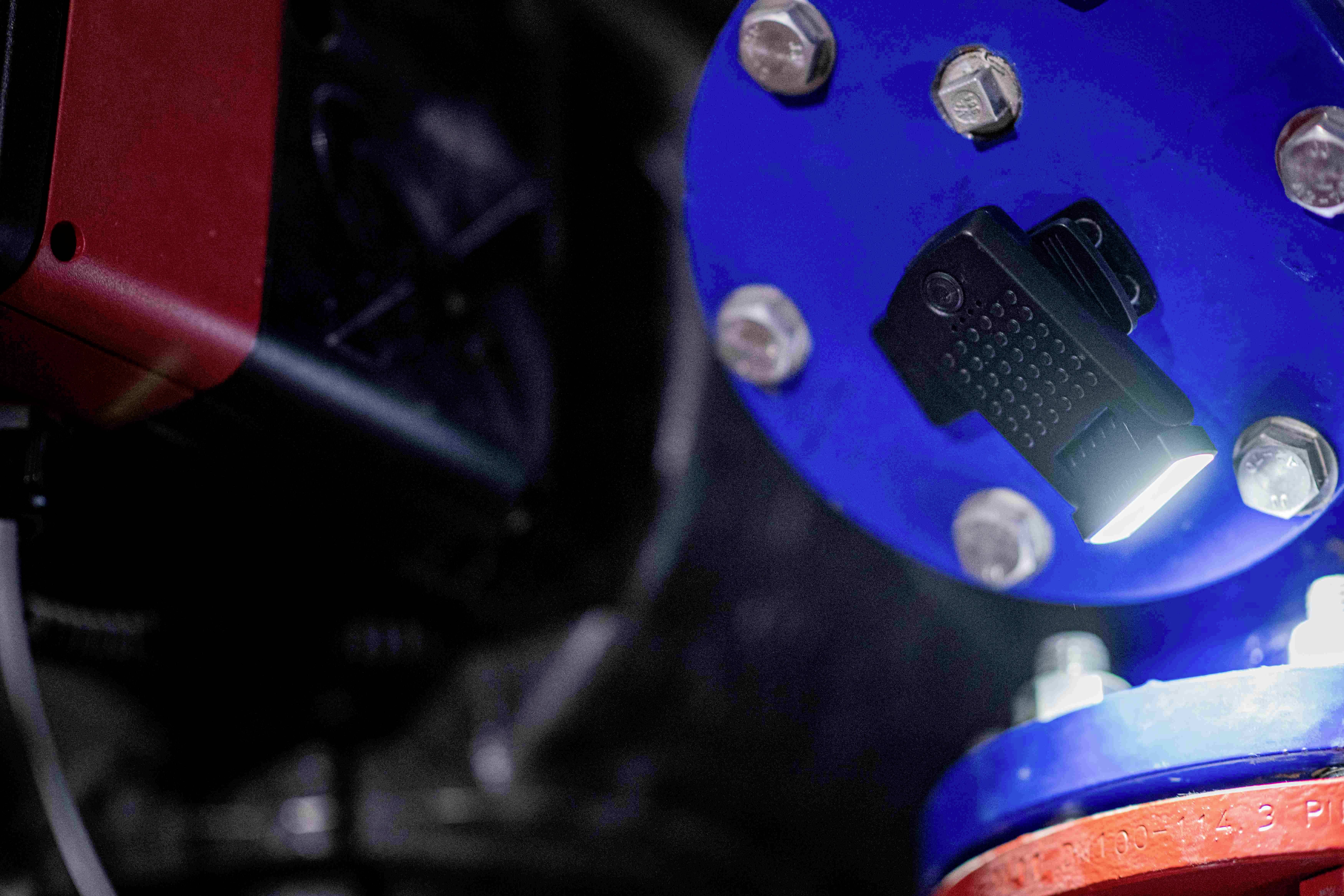 Nahaufnahme einer industriellen Rohrverbindung. Eine Lampe beleuchtet die Schrauben an einem blauen Rohrflansch in einer Fabrikumgebung.