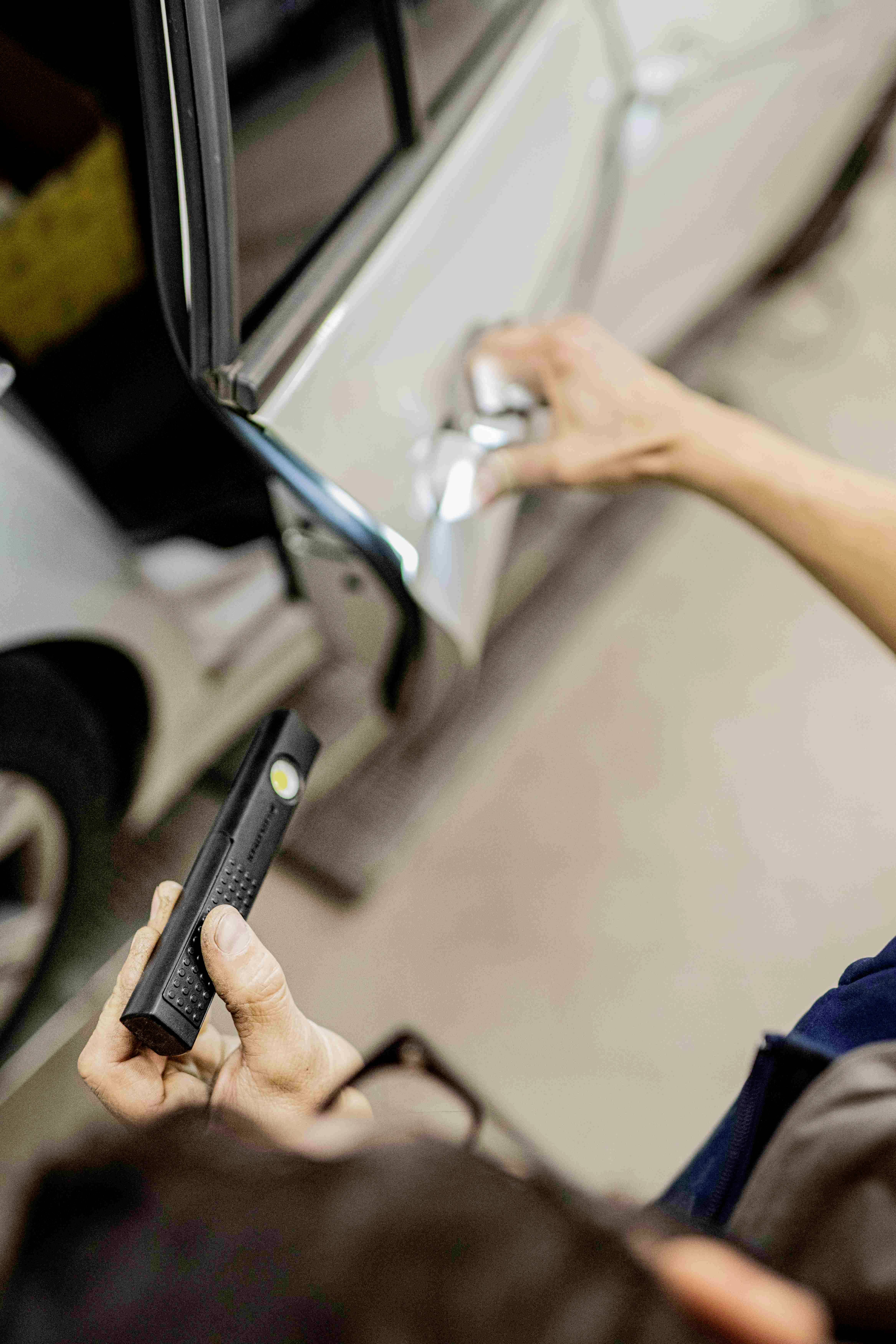 Person hält einen Lackdickenmesser an die Tür eines Autos, um die Lackdicke zu überprüfen.