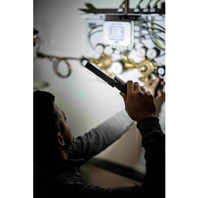 Ein Techniker repariert ein komplexes Rohrsystem mit Werkzeug, umgeben von Anzeigen und Reglern.
