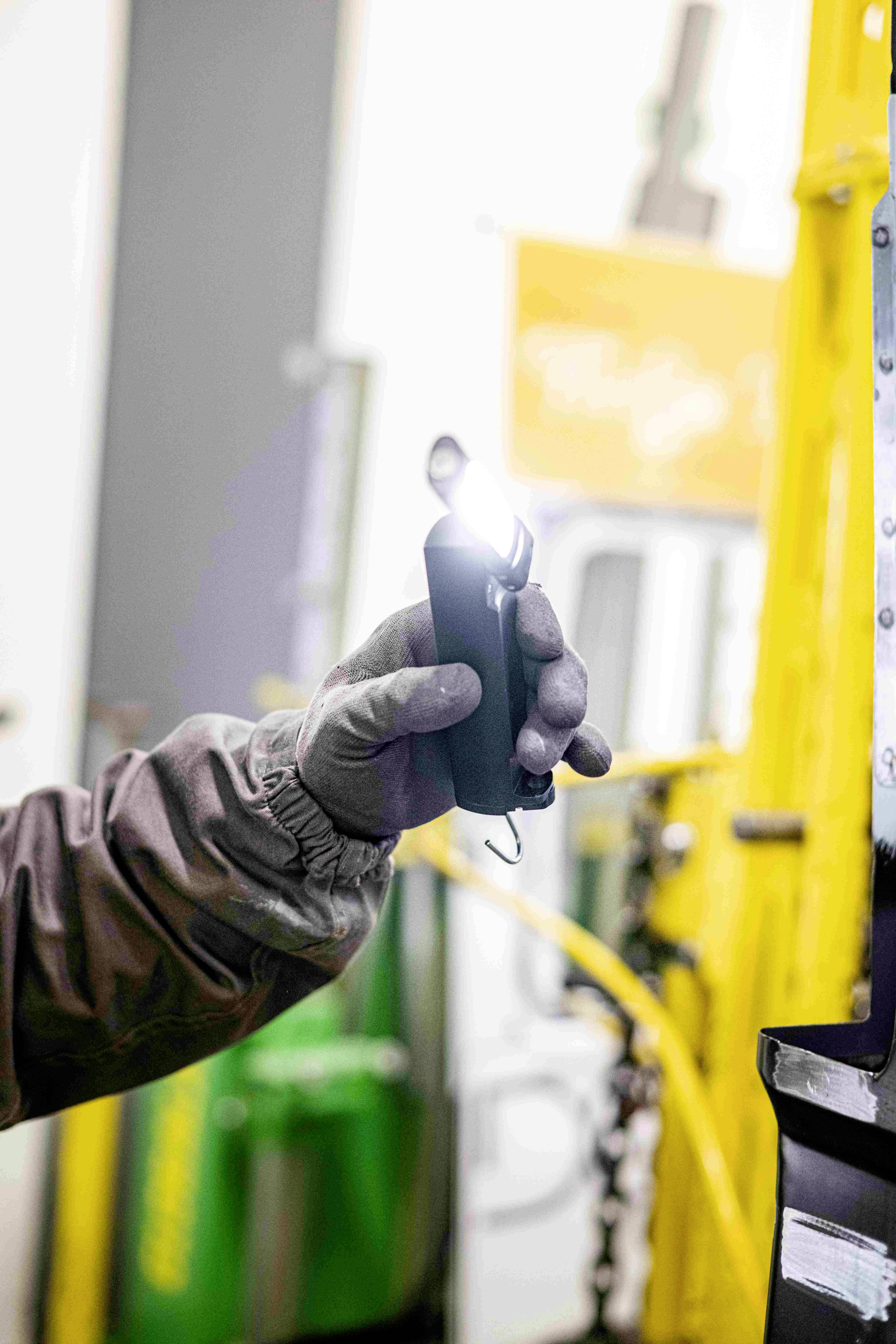 Eine Person hält eine kleine, leuchtende Taschenlampe in behandschuhter Hand, um ein Arbeitsgebiet in einer Werkstatt auszuleuchten.