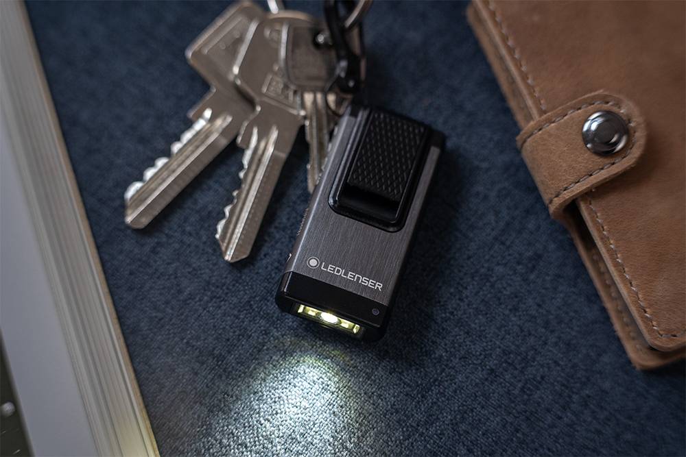 Eine kleine LED-Taschenlampe leuchtet auf ein Tischset und liegt neben einem Schlüsselbund und einer braunen Ledergeldbörse.