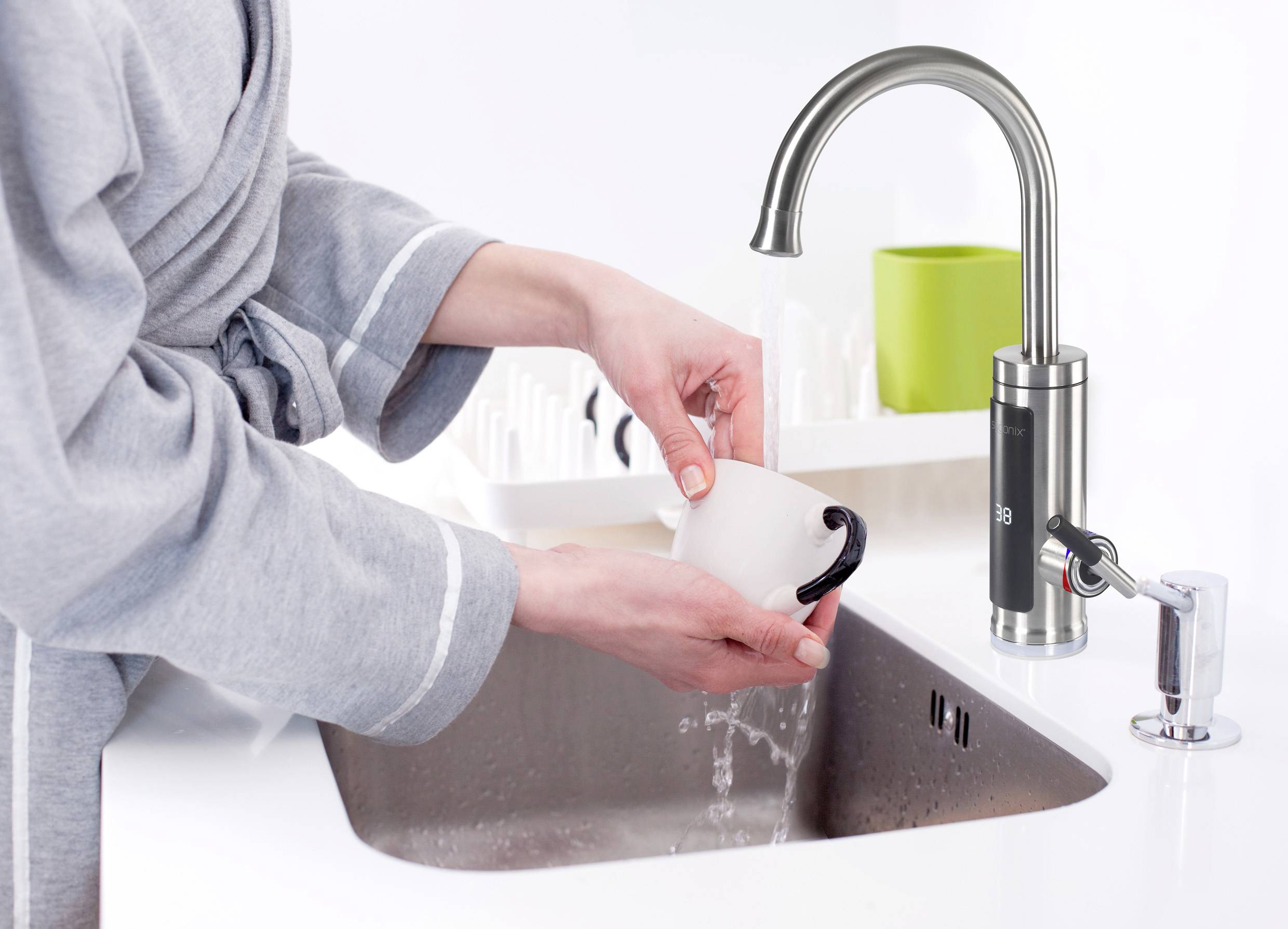 Eine Person in einem grauen Bademantel wäscht eine weiße Tasse unter fließendem Wasser an einem modernen Wasserhahn in der Küche.