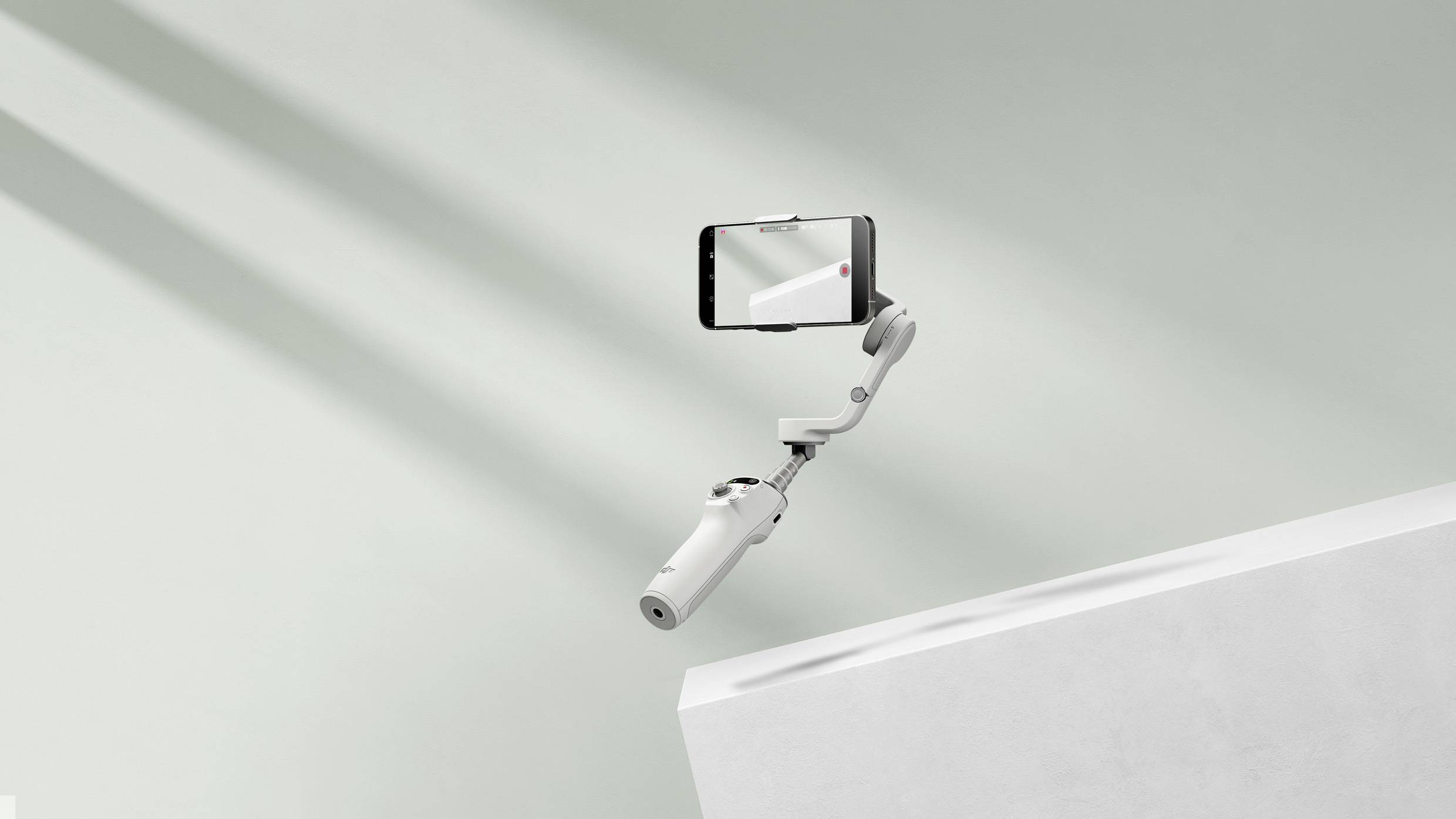 Ein Smartphone in einem Gimbal schwebt über einer weißen Kante vor einem hellen Hintergrund. Es wirkt modern und technologisch.