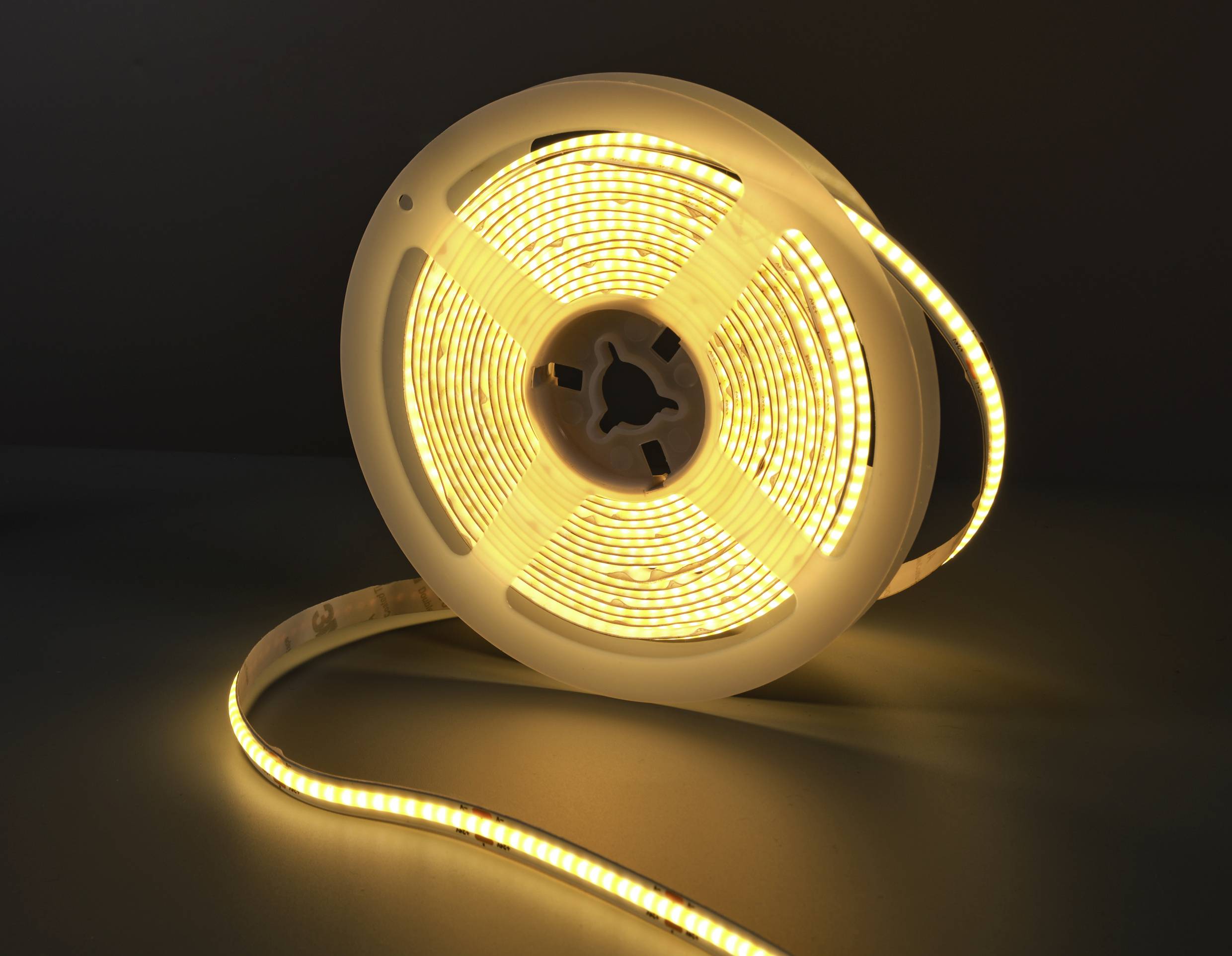 Eine aufgerollte LED-Lichterkette, die warmweiß leuchtet, liegt auf einem dunklen Hintergrund.