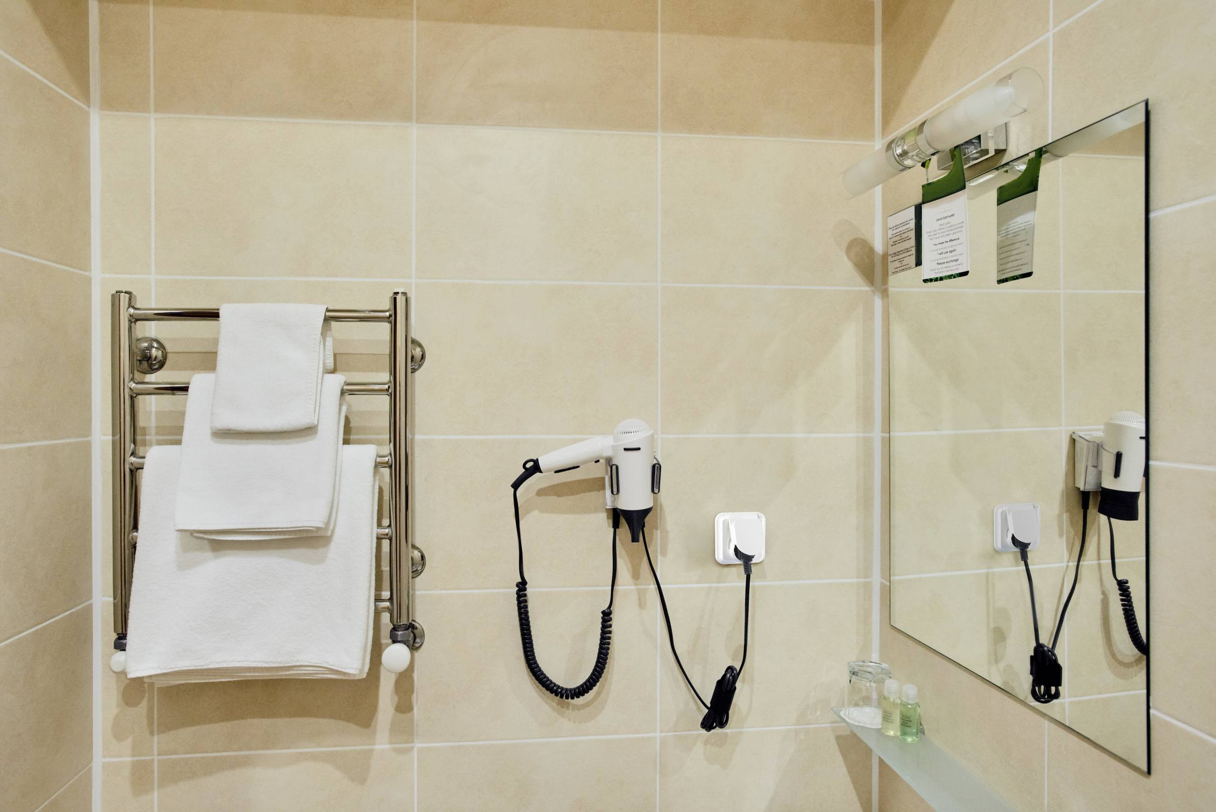 Badezimmer mit Handtuchhalter, weißen Handtüchern, Wandfön und Spiegel.