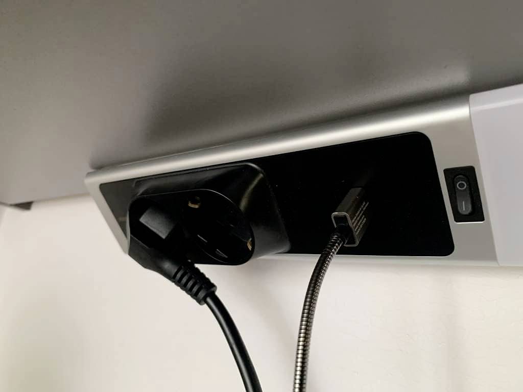 Steckdose unter einem Tisch mit zwei Anschlüssen: ein Eurostecker und ein USB-Kabel sind eingesteckt.