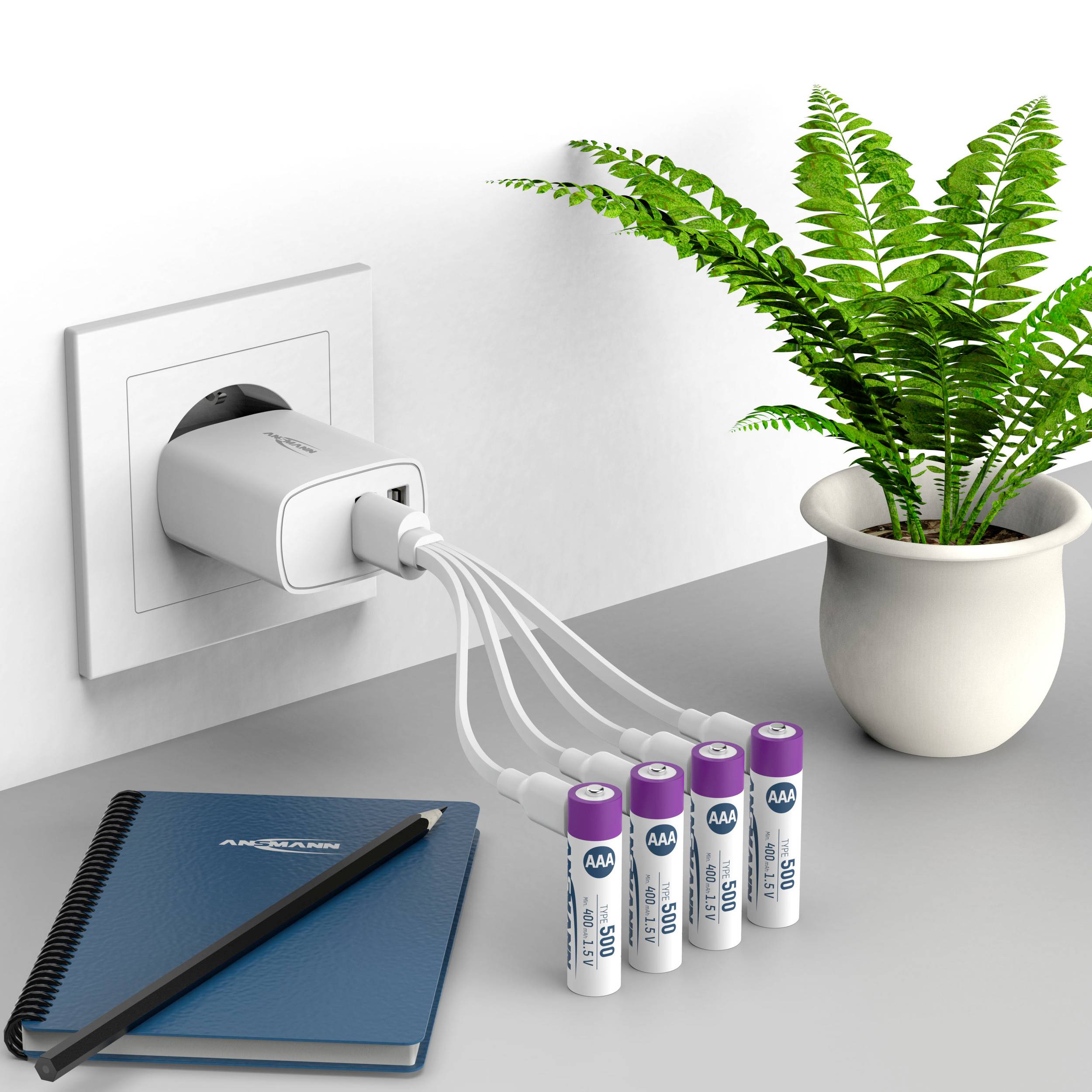 Ein Ladegerät steckt in einer Steckdose. Vier AA-Batterien sind über Kabel angeschlossen. Daneben stehen ein Notizbuch und eine grüne Pflanze.