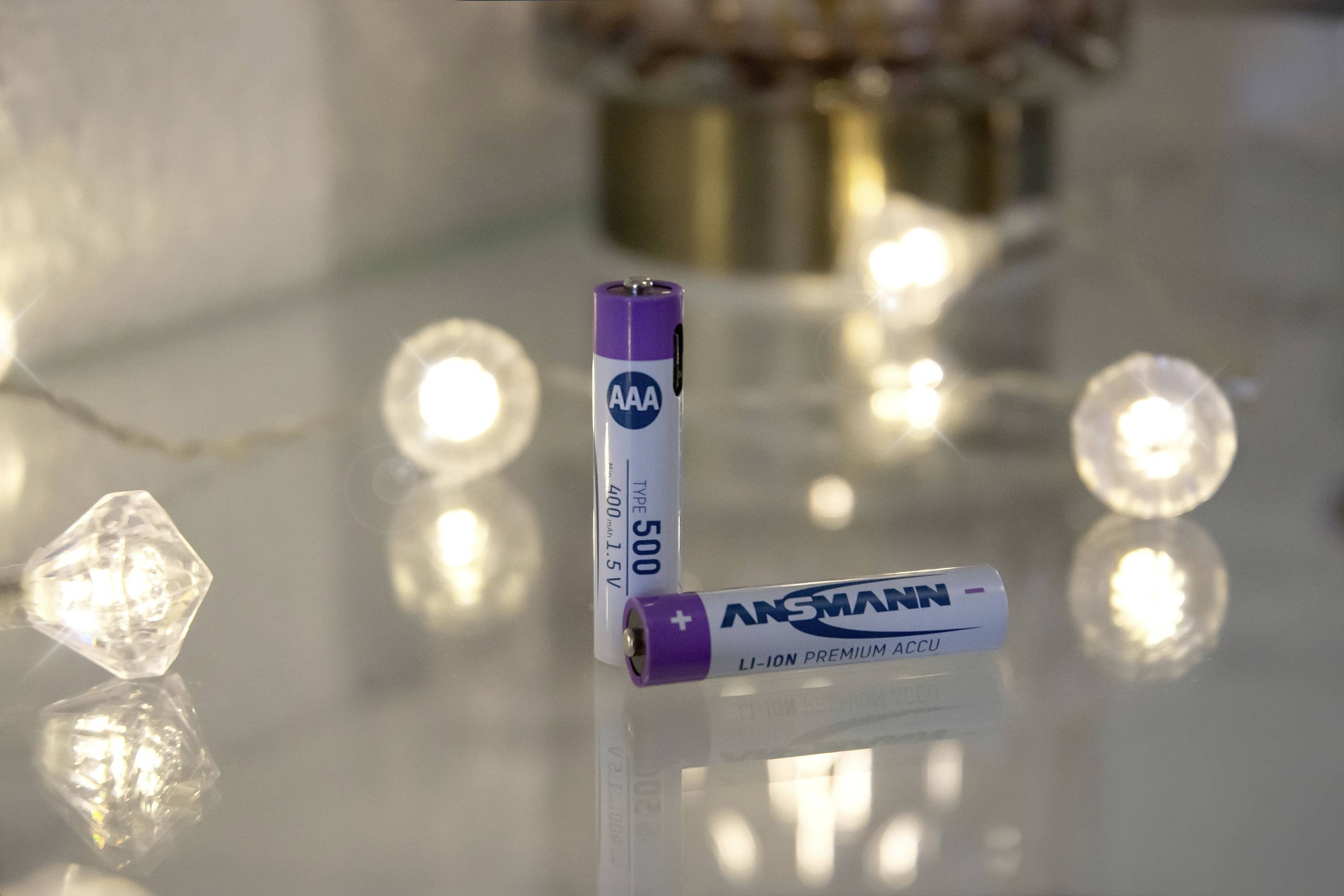 Zwei AA-Batterien stehen auf einer spiegelnden Oberfläche, umgeben von kleinen, leuchtenden Kugeln.