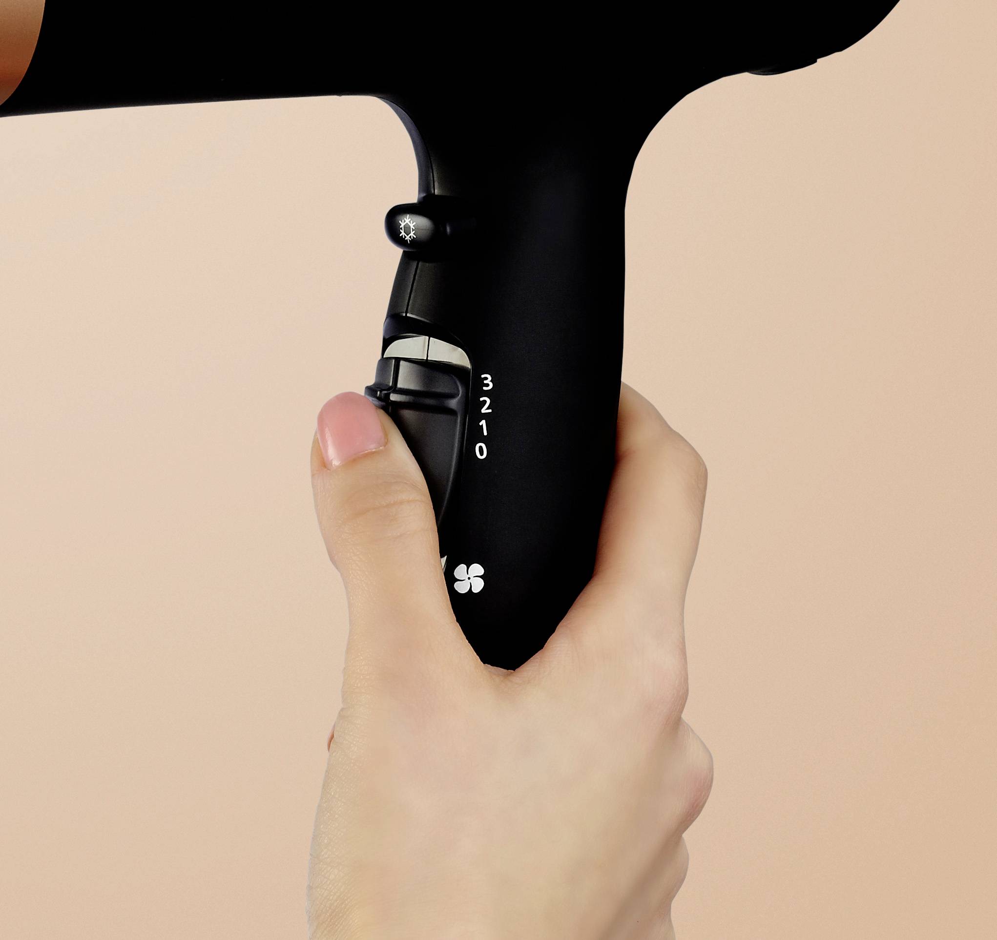 Eine Hand hält einen schwarzen Haartrockner. Die Bedienelemente am Griff zeigen die Einstellungen von 0 bis 3.
