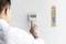 Ein Mann bedient ein digitales Thermostat. Daneben hängt ein traditionelles Thermometer an der Wand und zeigt die Raumtemperatur an.