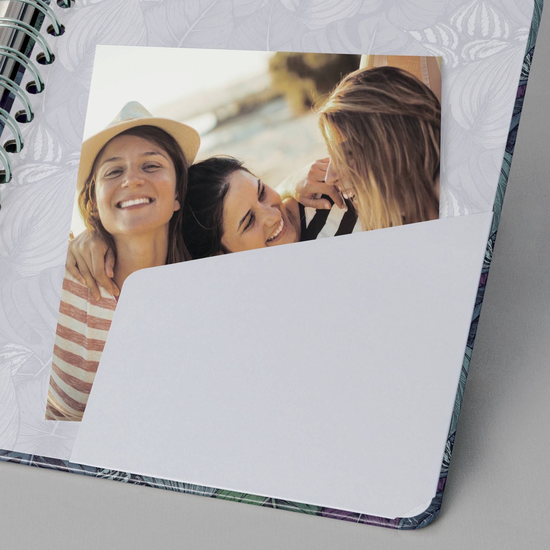 Ein aufgeschlagenes Notizbuch mit einem Foto, das drei lachende Menschen zeigt, die sich umarmen. Eine trägt einen Hut.