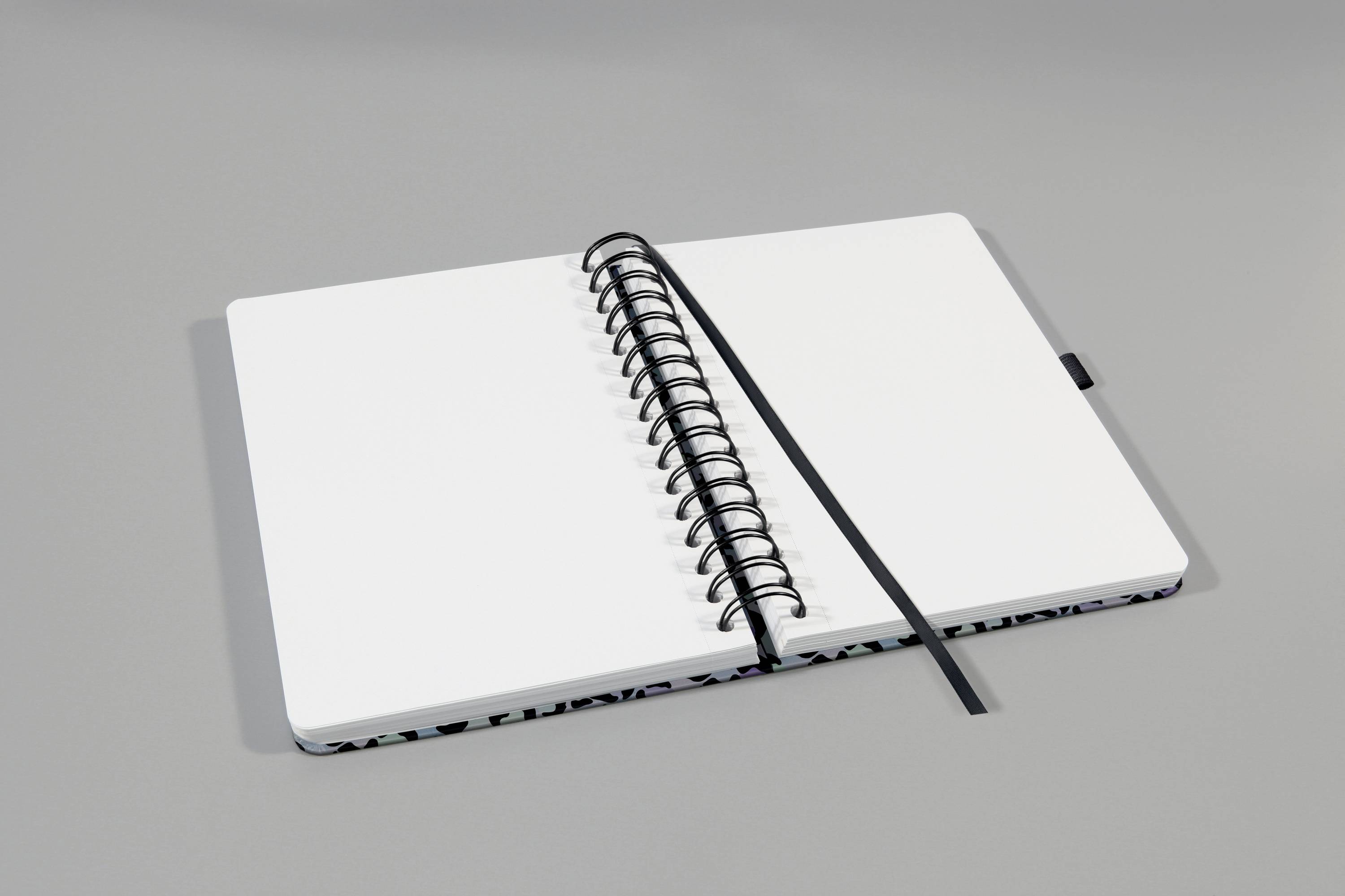 Ein offenes Notizbuch mit weißen, leeren Seiten und einem schwarzen Lesezeichen liegt auf einem grauen Hintergrund.