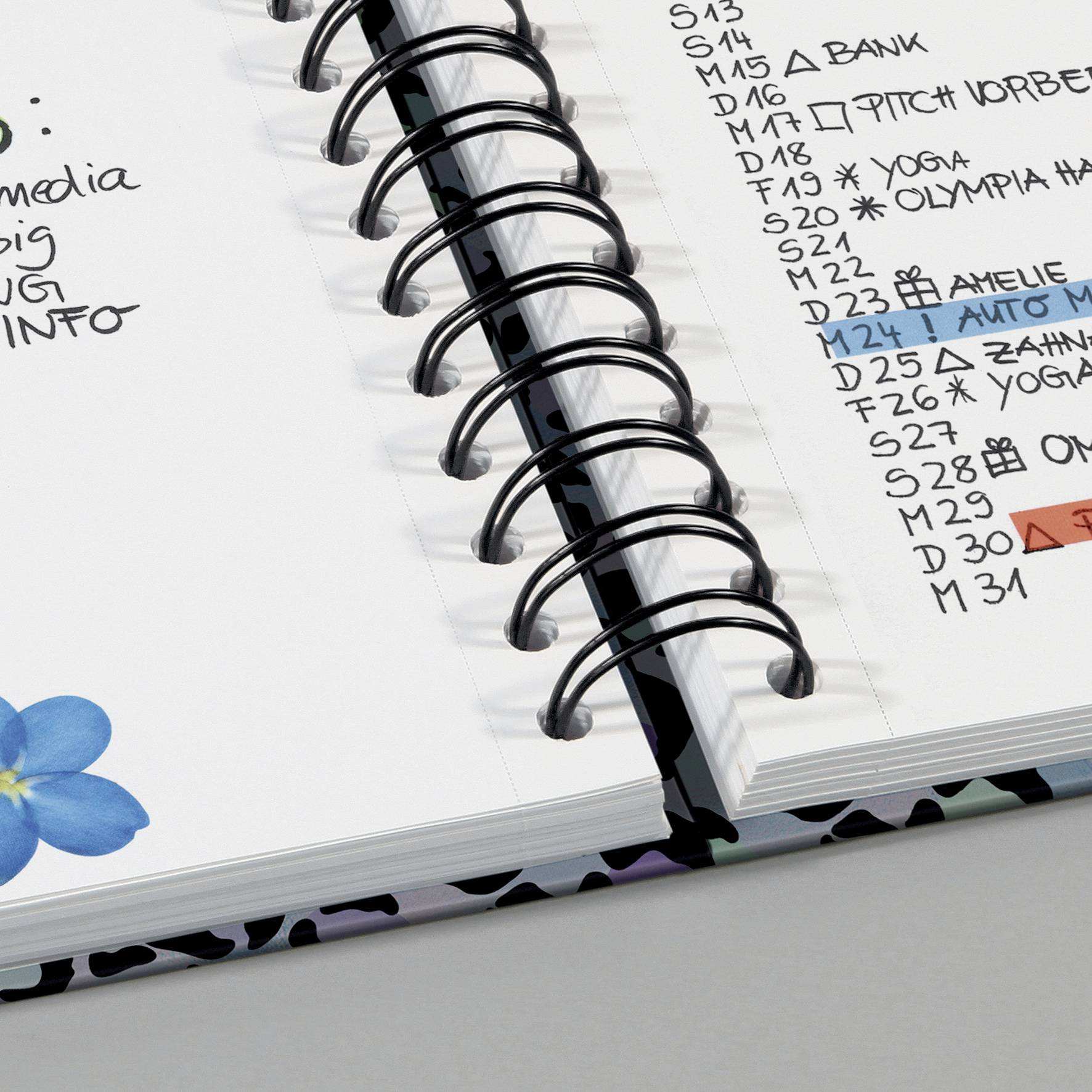 Seite eines Planers mit handschriftlichen Notizen, darunter Termine und Erinnerungen. Eine blaue Blume ist unten links abgebildet.