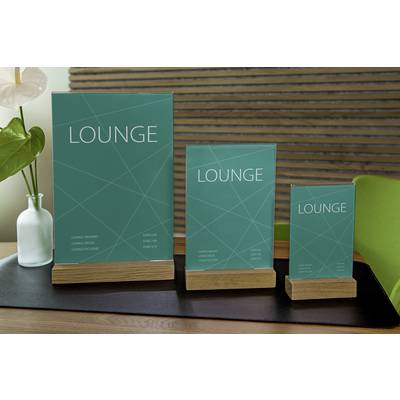 Drei türkisfarbene Tischaufsteller mit dem Text 'LOUNGE' stehen auf Holzsockeln vor einer hölzernen Wand. Sie sind unterschiedlich groß.