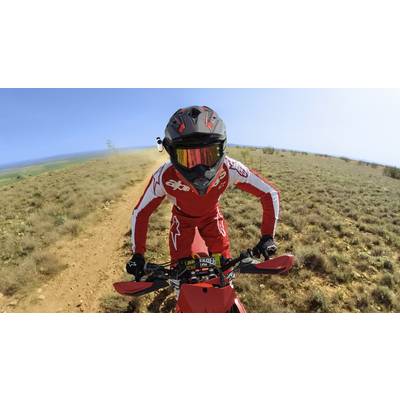 Eine Person in rotem Anzug und Helm fährt mit einem Motorrad über einen staubigen Feldweg in einer offenen Landschaft.