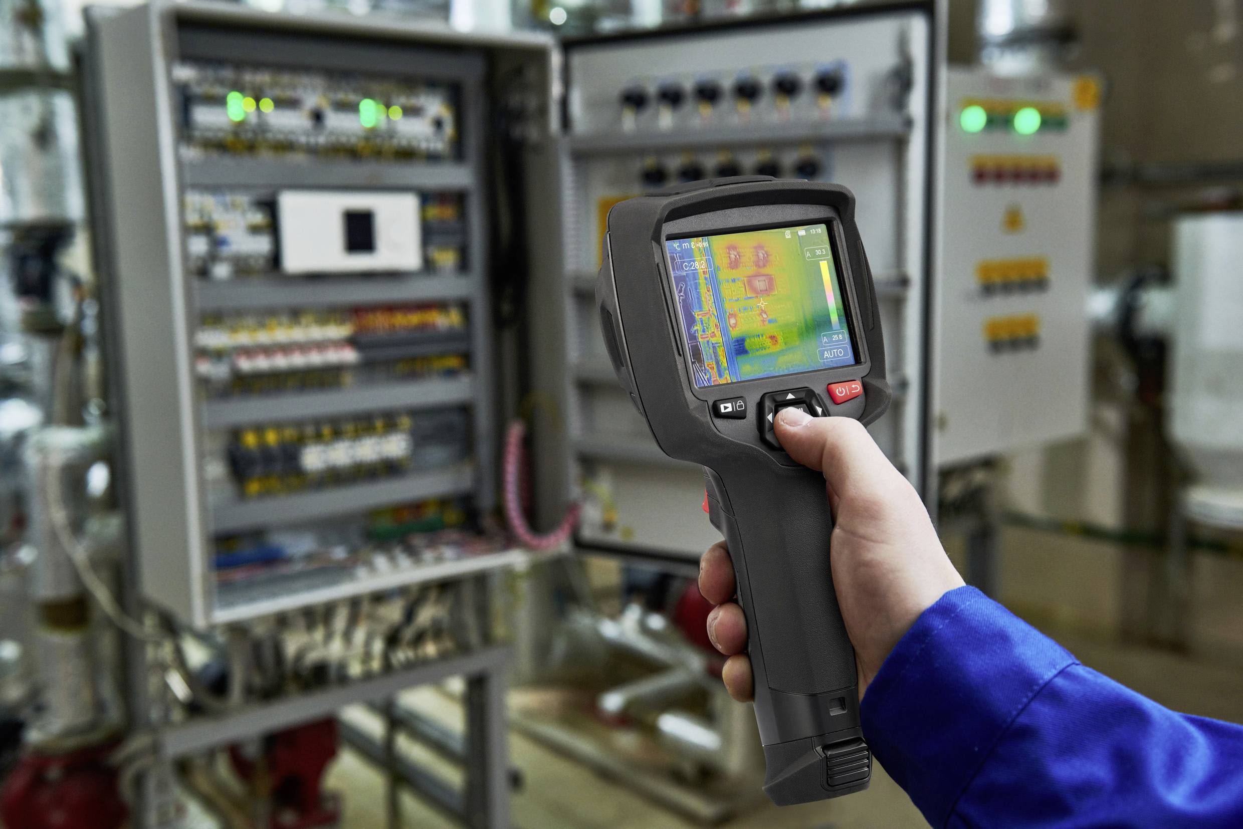 Eine Person misst mit einem Handscanner die Temperatur elektrischer Schaltschränke in einer industriellen Umgebung.