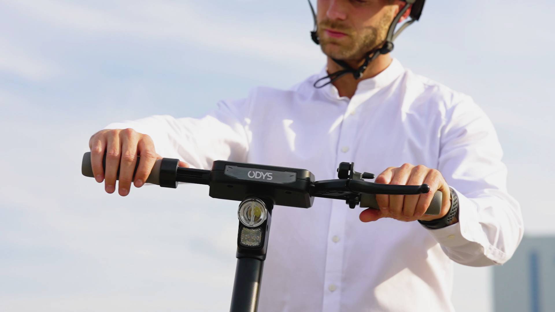 Eine Person mit Helm hält den Lenker eines Elektrorollers und steht draußen bei sonnigem Wetter.
