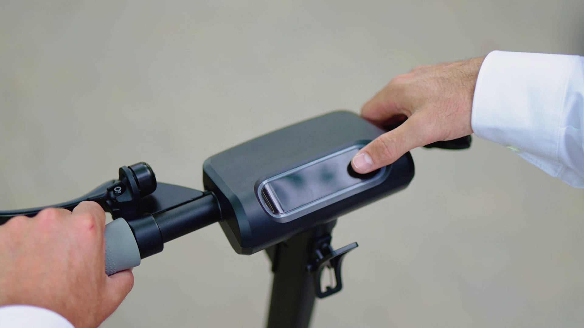 Nahaufnahme von zwei Händen, die den Lenker eines Elektrorollers halten. Eine Hand zeigt auf ein Display in der Mitte des Lenkers.