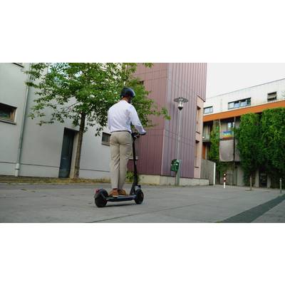 Ein Mann mit Helm fährt auf einem E-Scooter auf einem Bürgersteig in einer Wohngegend. Im Hintergrund sind Gebäude und Bäume zu sehen.
