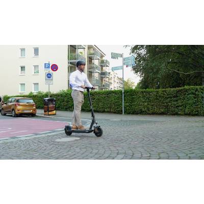 'Person fährt mit einem Elektroroller auf einem Bürgersteig in einer Wohngegend. Wohnungskomplex und Verkehrsschilder im Hintergrund.'