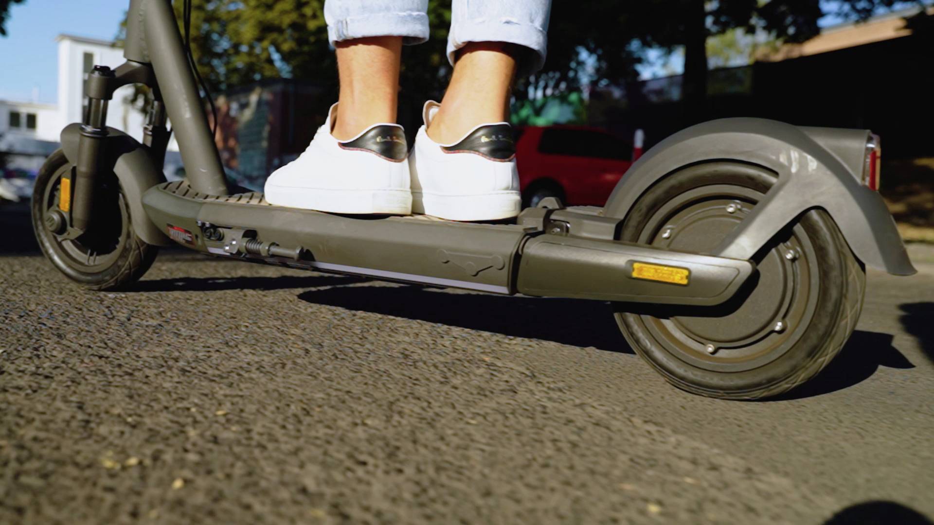 Ein Elektroroller auf einer Straße mit einer Person, die weiße Sportschuhe trägt, zeigt aktive Fortbewegung in urbaner Umgebung.