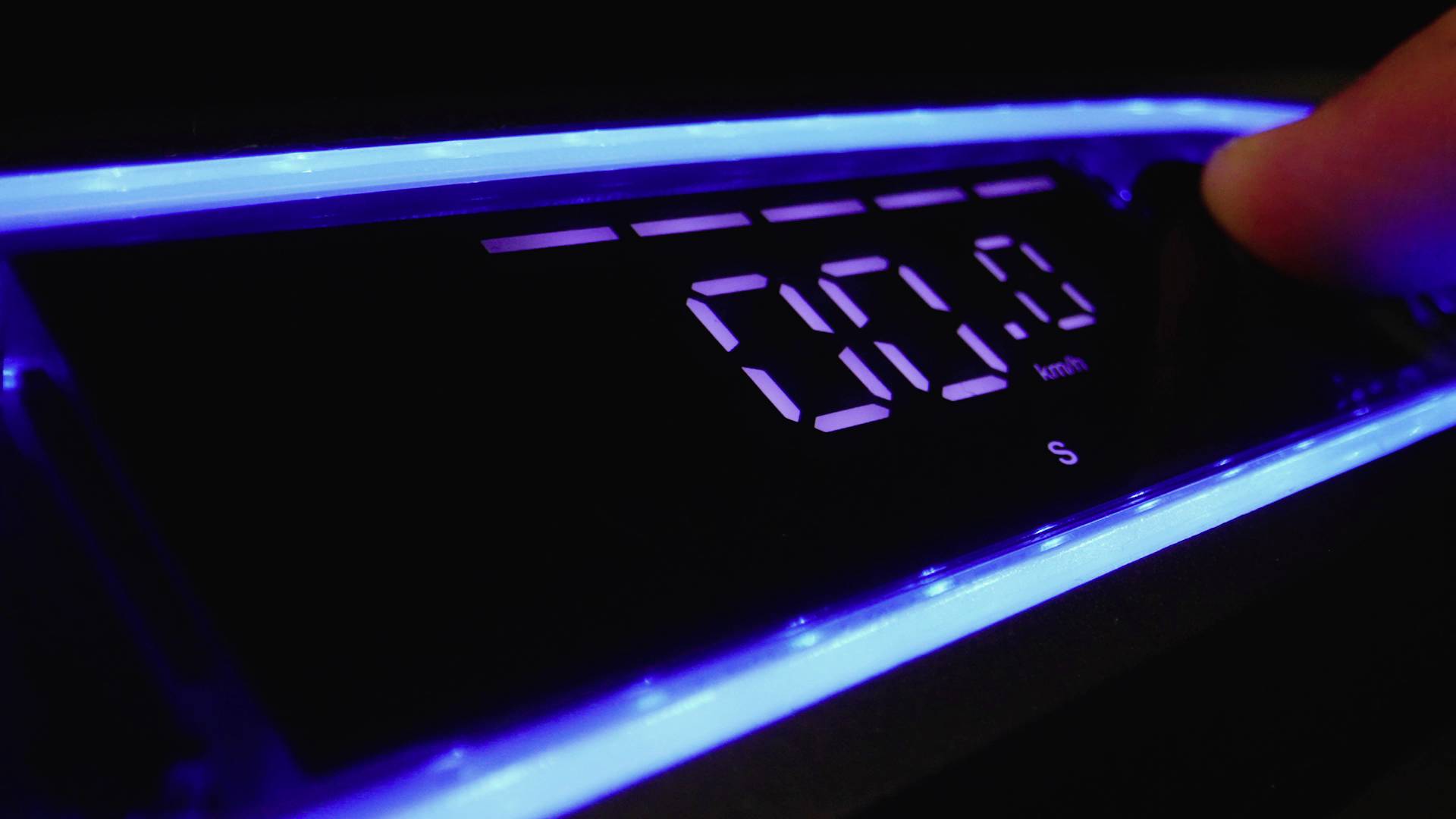 Ein digitaler Bildschirm zeigt '00:00' an, umgeben von blauem Licht. Eine Hand betätigt einen Knopf rechts daneben.