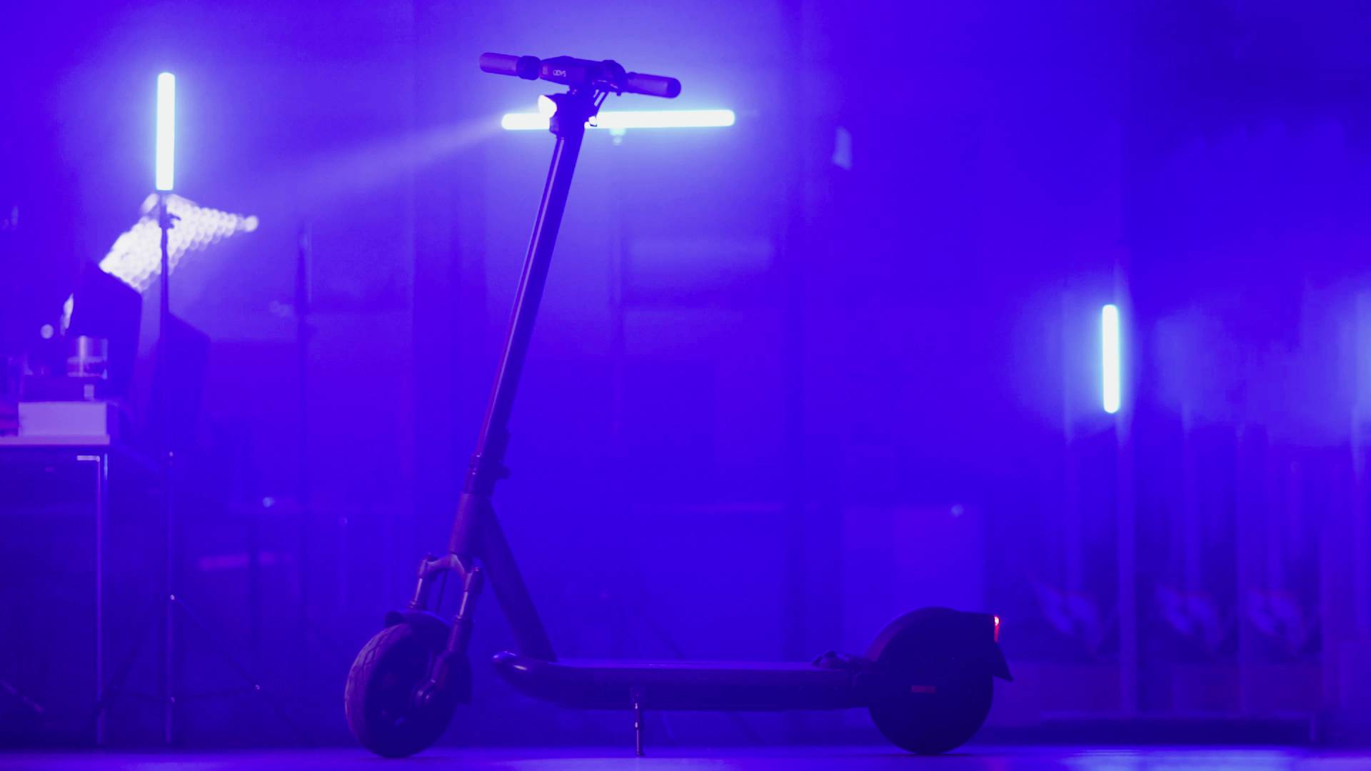 Ein E-Scooter steht in einem blau beleuchteten Raum. Im Hintergrund sind verschiedene Lichter und Schatten erkennbar.