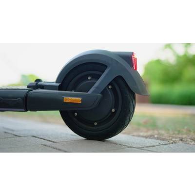 Ein elektrischer Scooter steht auf einem Gehweg. Der Fokus liegt auf dem Hinterrad mit Bremslicht und Straßenumgebung im Hintergrund.