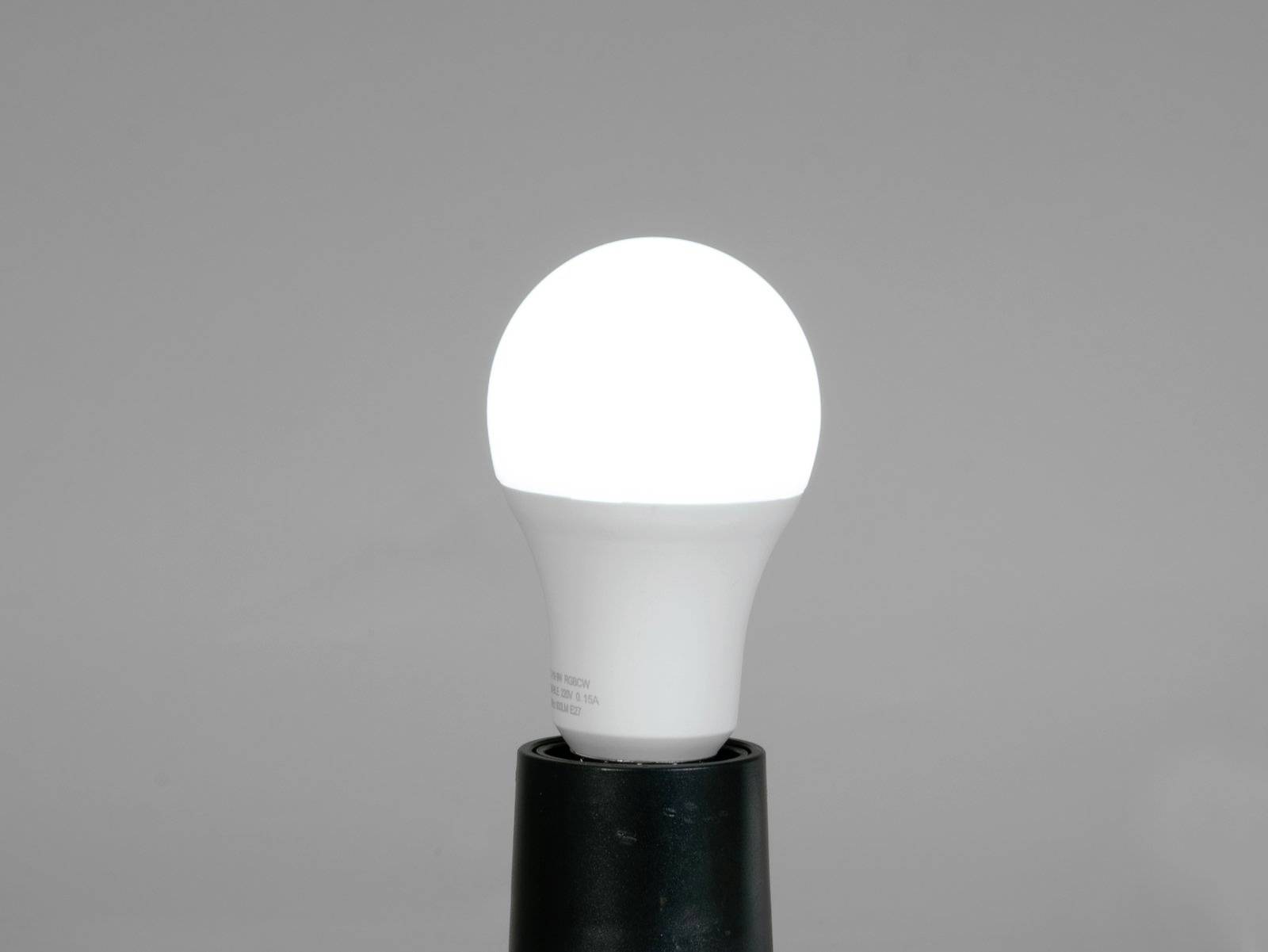 Eine eingeschaltete LED-Glühbirne auf grauem Hintergrund. Sie leuchtet hell und ist in einer schwarzen Fassung angebracht.