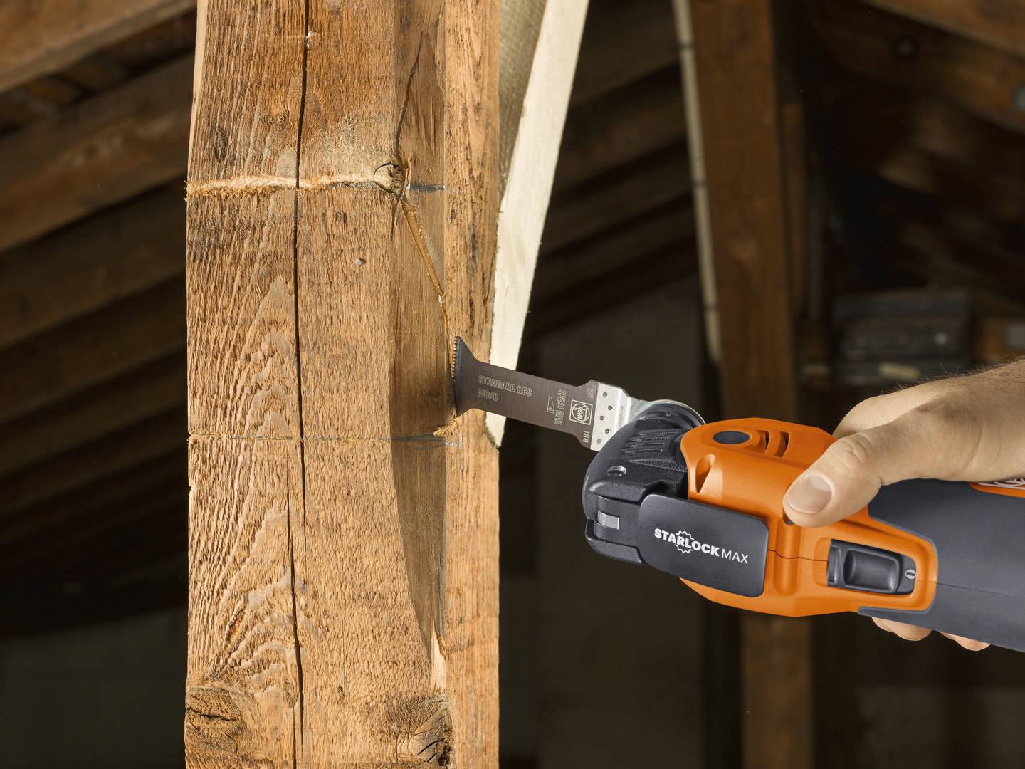 Eine Hand hält ein oszillierendes Multitool, das einen Holzbalken sägt. Der Raum wirkt handwerklich und rustikal.