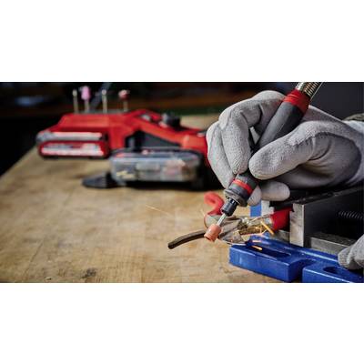 Eine Person trägt Handschuhe und führt präzises Löten an einem Metallstück auf einer Werkbank durch. Im Hintergrund ist ein rotes Werkzeug sichtbar.