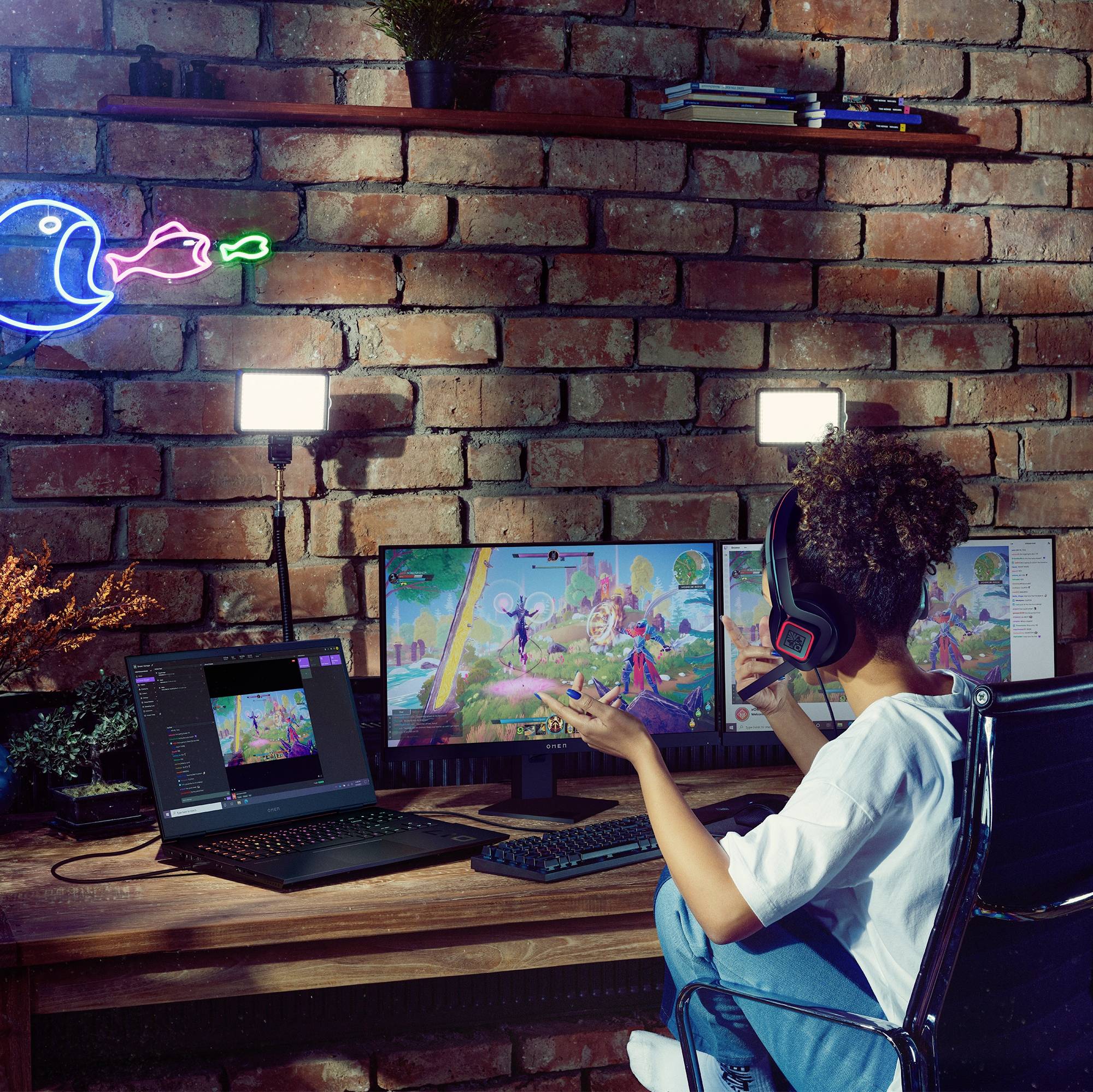 Junge Frau mit Kopfhörern spielt ein Videospiel auf einem Computer in einem beleuchteten Raum mit einem Neon-Pac-Man an der Wand.