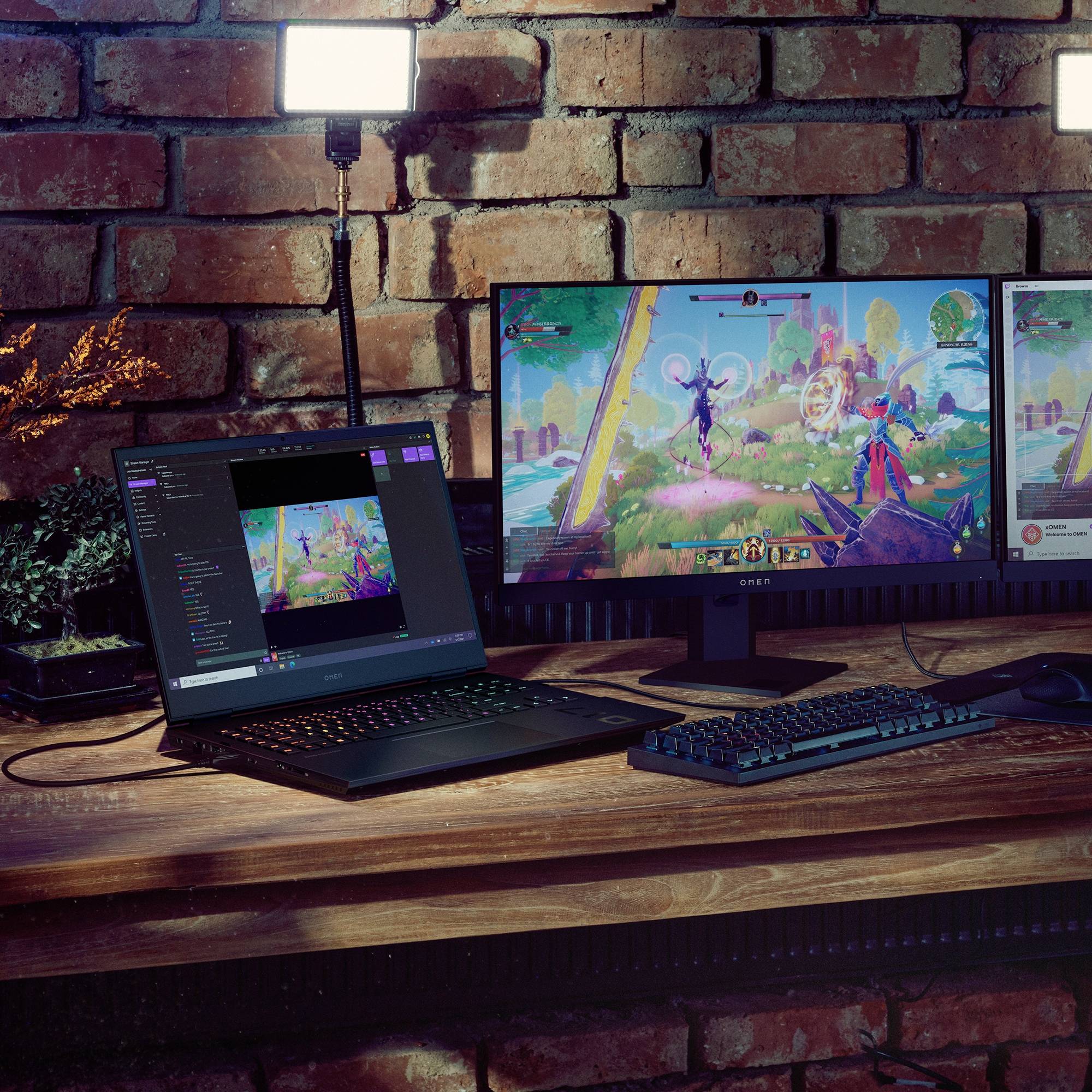 Ein Computer-Setup mit Monitoren zeigt ein buntes Videospiel. Eine Kamera und Beleuchtung sind vorhanden, was auf ein Streaming-Setup hinweist.