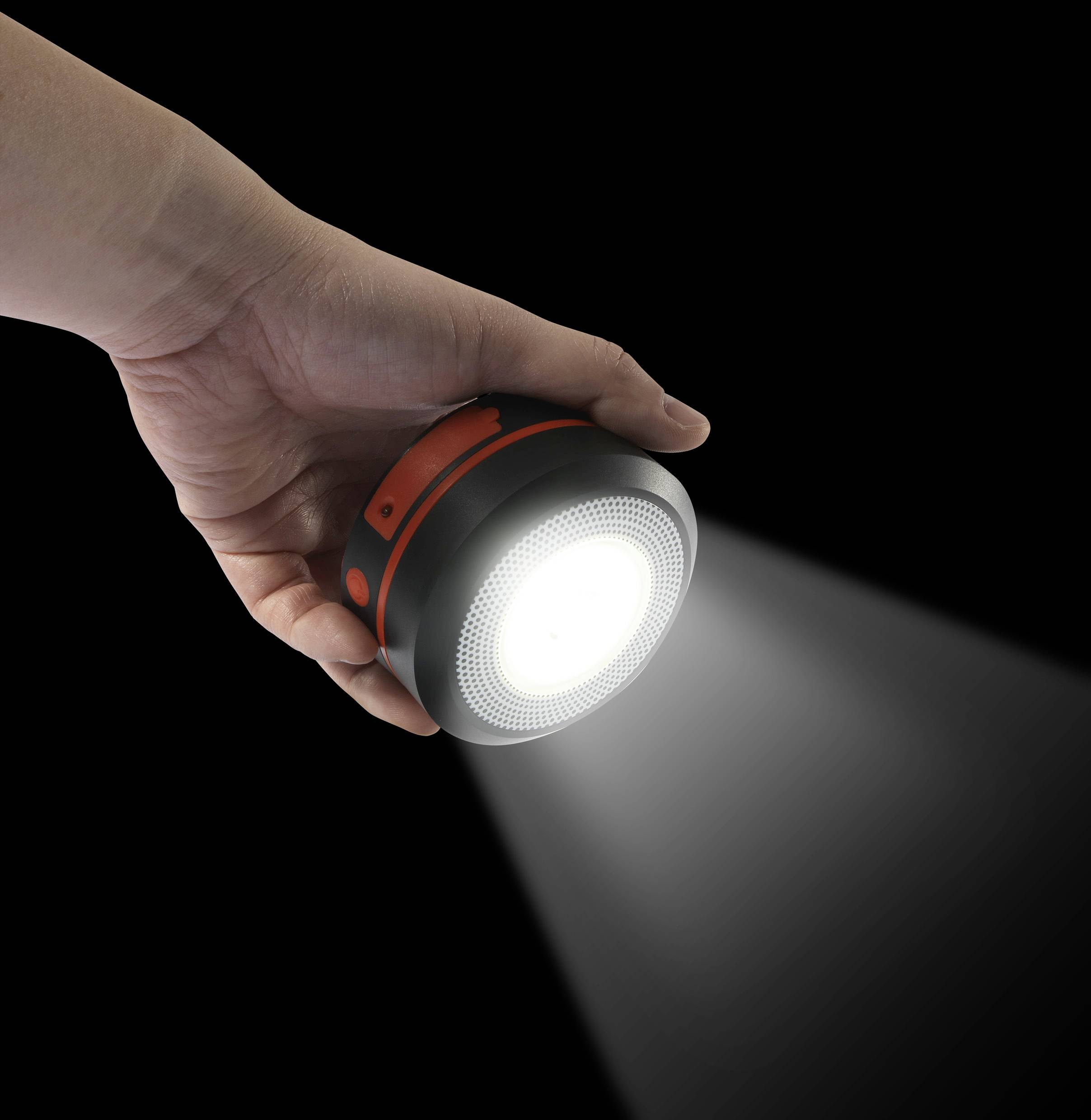 Hand hält eine runde, leuchtende Taschenlampe, die helles Licht ausstrahlt. Der Hintergrund ist schwarz, was den Lichtschein betont.