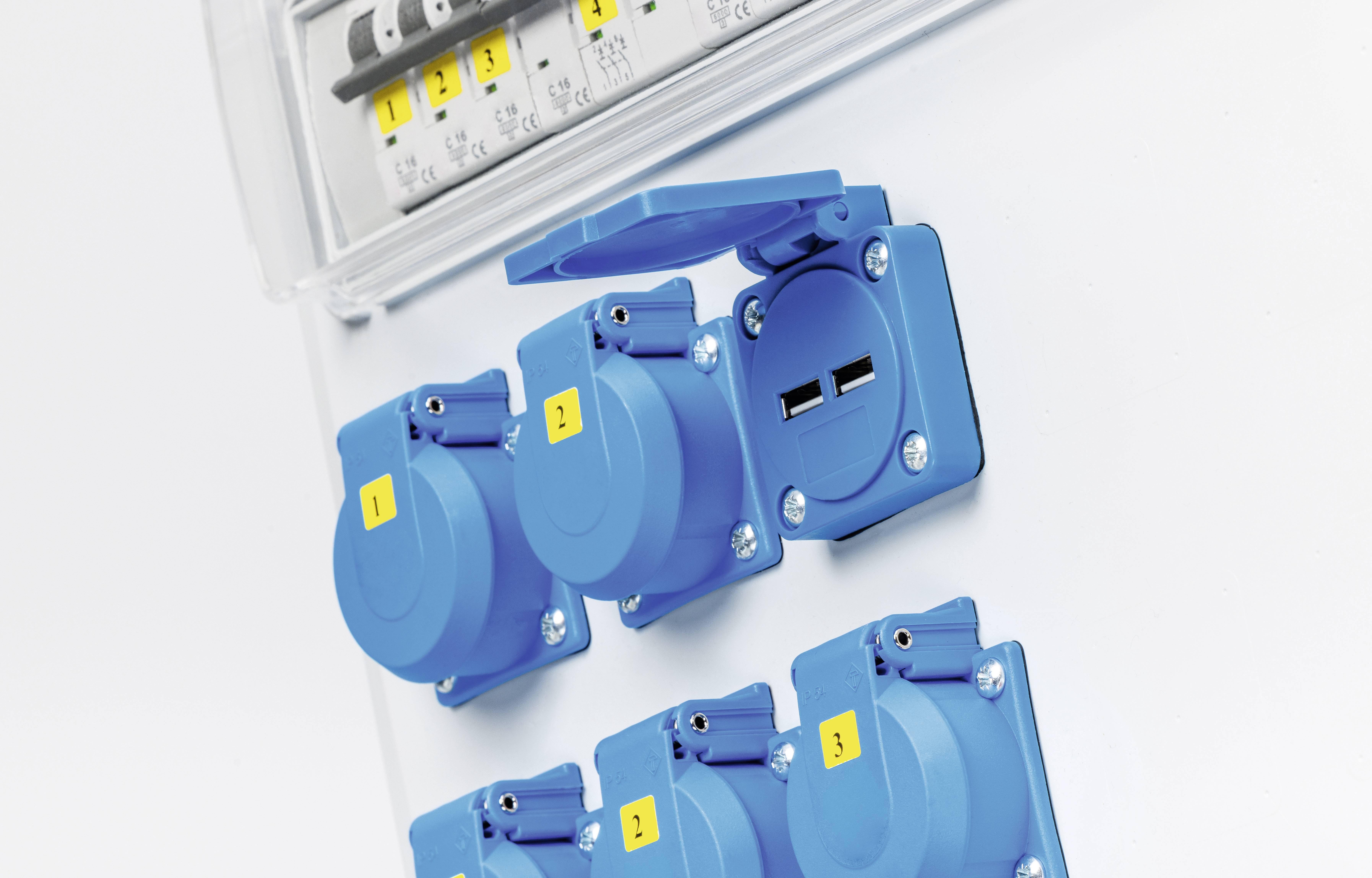 Ein elektrisches Schaltpanel mit mehreren blauen Steckdosen und zwei USB-Anschlüssen an einer weißen Wand.