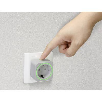 'Finger zeigt auf eine intelligente Steckdose mit leuchtendem grünem Ring in einer Wandsteckdose installiert.'