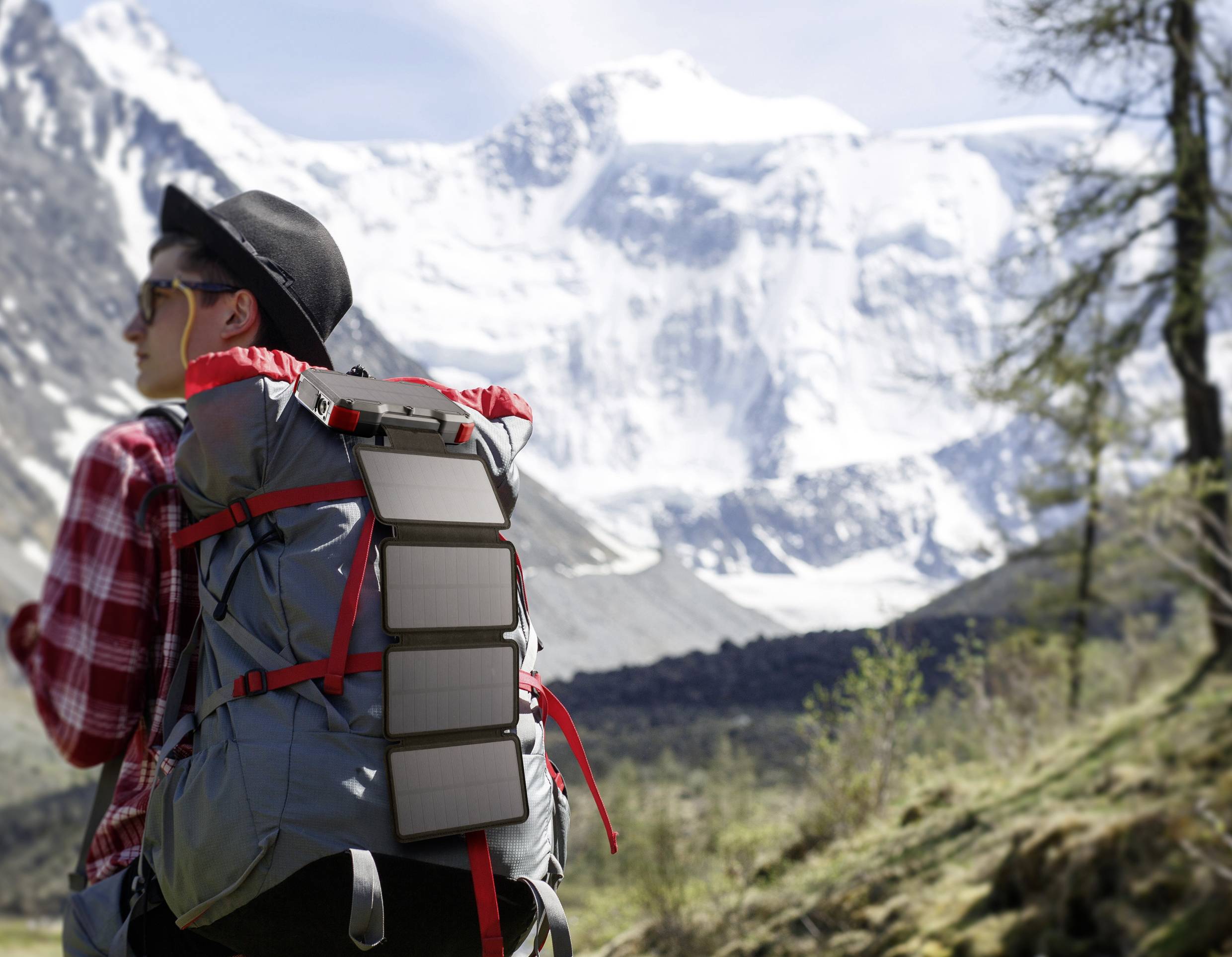 Eine Person wandert mit einem Rucksack und tragbarem Solarpanel in einer verschneiten Berglandschaft.