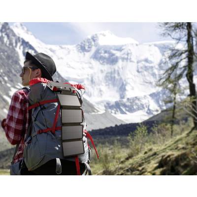 Eine Person wandert mit einem Rucksack und tragbarem Solarpanel in einer verschneiten Berglandschaft.