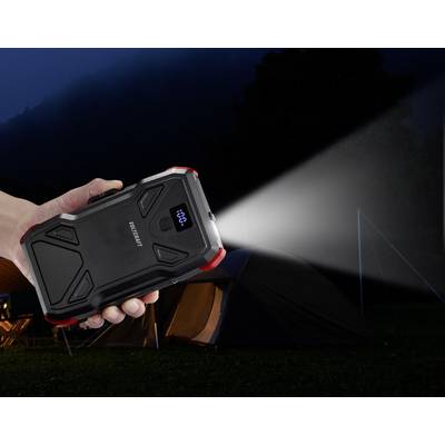 Eine Hand hält eine tragbare Powerbank, die auch als Taschenlampe verwendet wird. Ein Zelt steht im Hintergrund bei Dunkelheit.