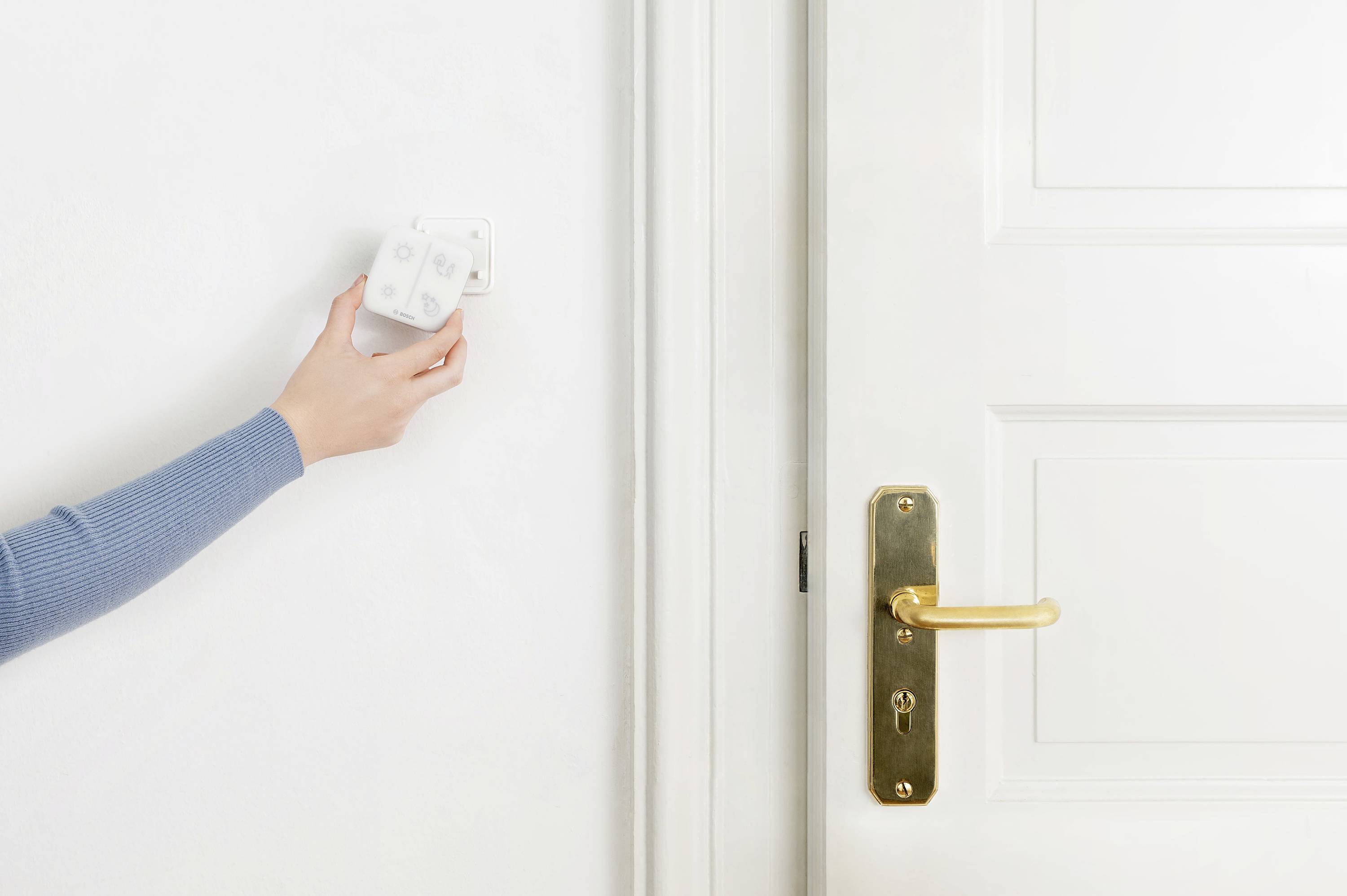 Eine Hand justiert einen Thermostat an der Wand neben einer weißen Tür mit goldener Klinke.