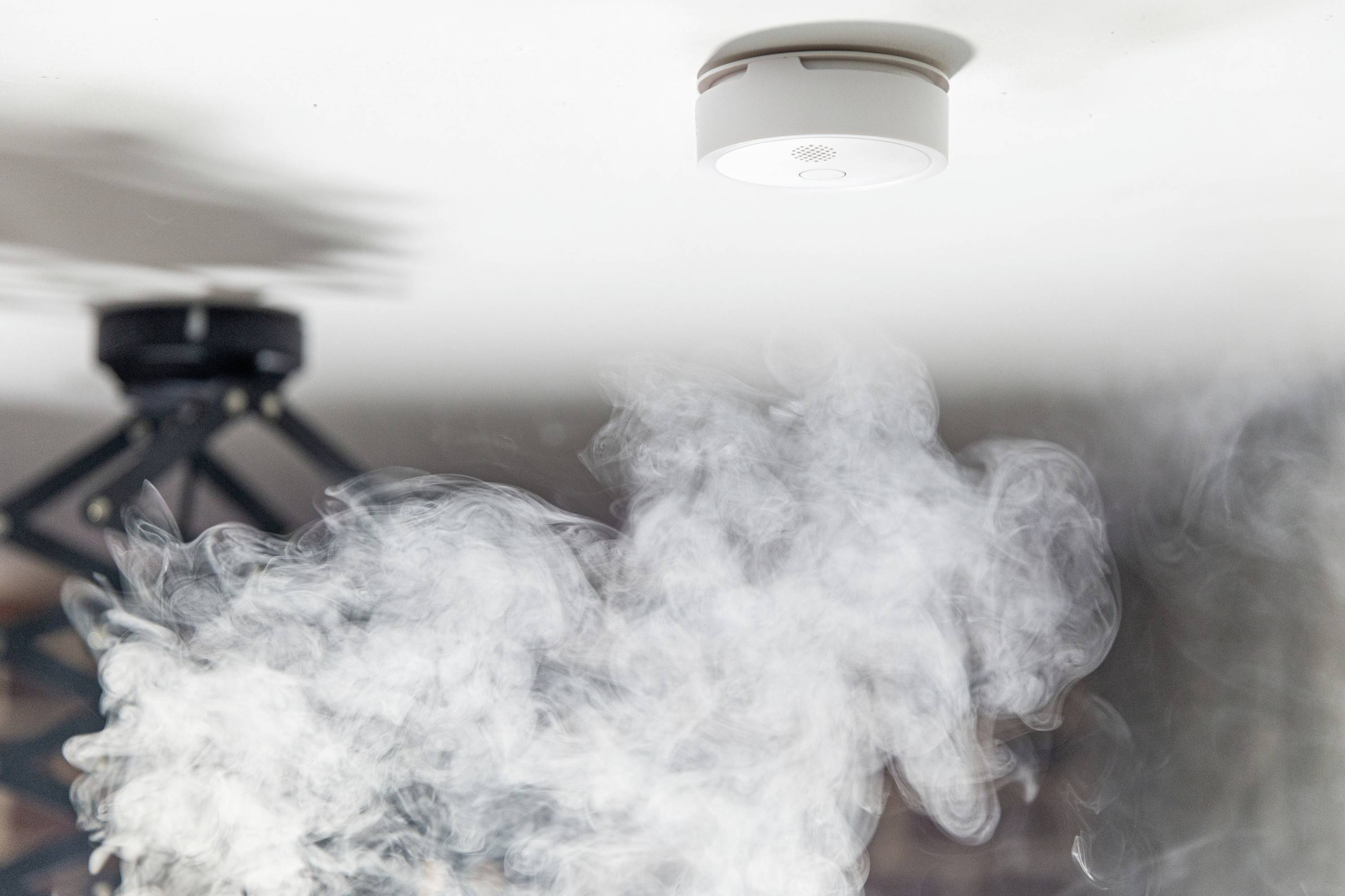 Rauchmelder an der Decke mit aufsteigendem Rauch, der Alarm auslöst.