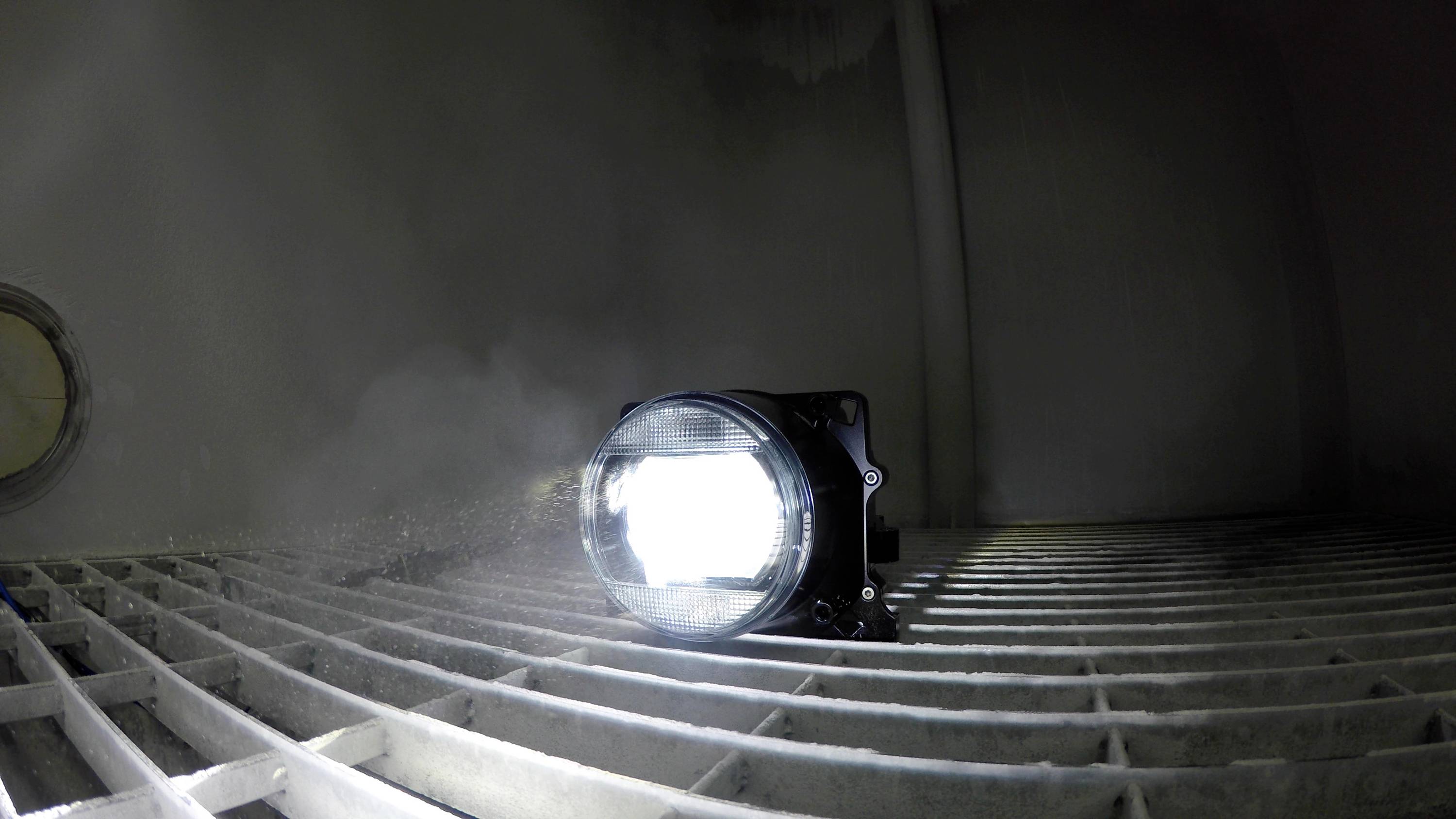 Ein Scheinwerfer leuchtet in einem düsteren Raum mit Gitterboden. Licht strahlt nach vorne und verbreitet ein intensives Leuchten.