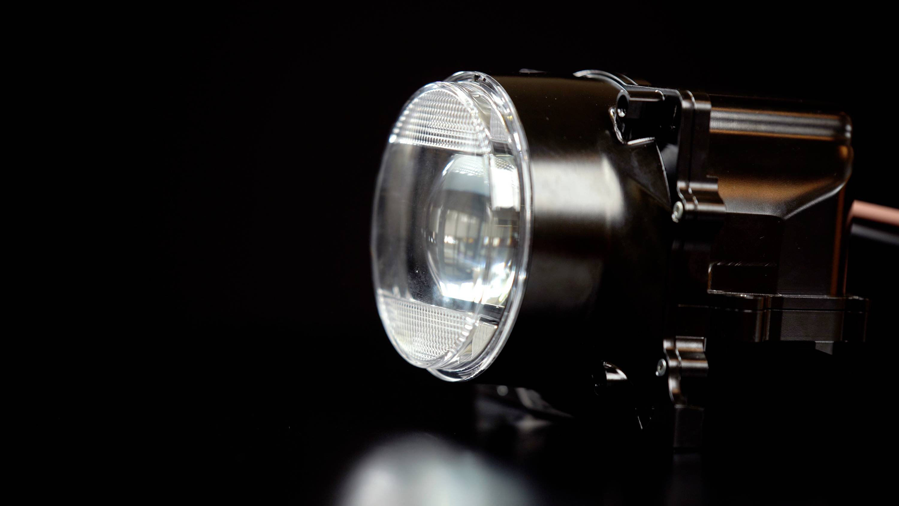 Nahaufnahme eines Autosscheinwerfers mit glänzender Glaslinse, platziert vor einem dunklen Hintergrund.