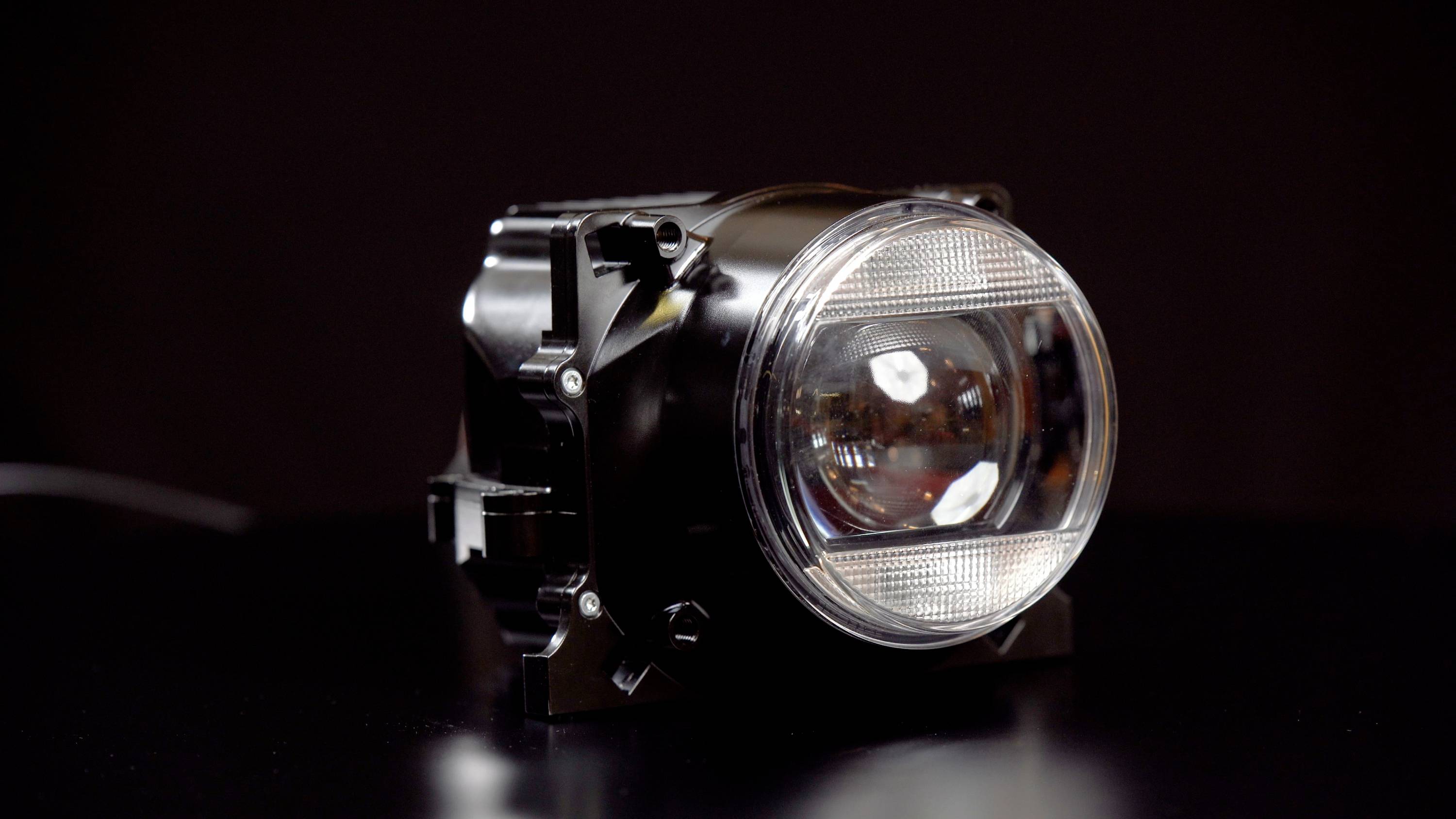 Schwarzer, zylindrischer Autoscheinwerfer mit klarem Reflektor und Linse auf dunklem Hintergrund.