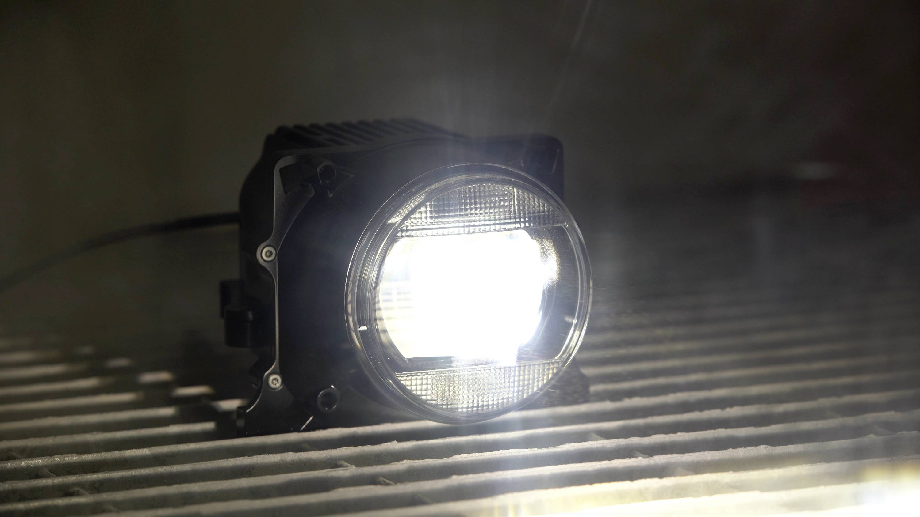 Ein beleuchteter Strahler auf einer gerippten Oberfläche, der helles Licht in einen dunklen Raum projiziert.