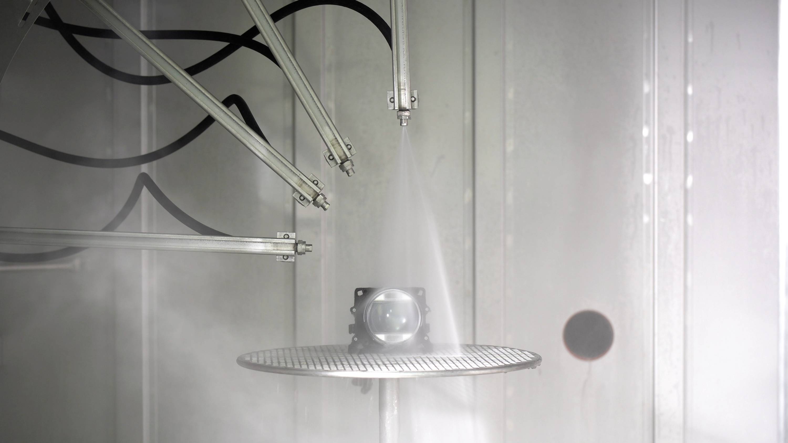 Eine Kamera wird in einer Testkammer von mehreren Düsen mit Wasser besprüht, um ihre Wasserbeständigkeit zu prüfen.