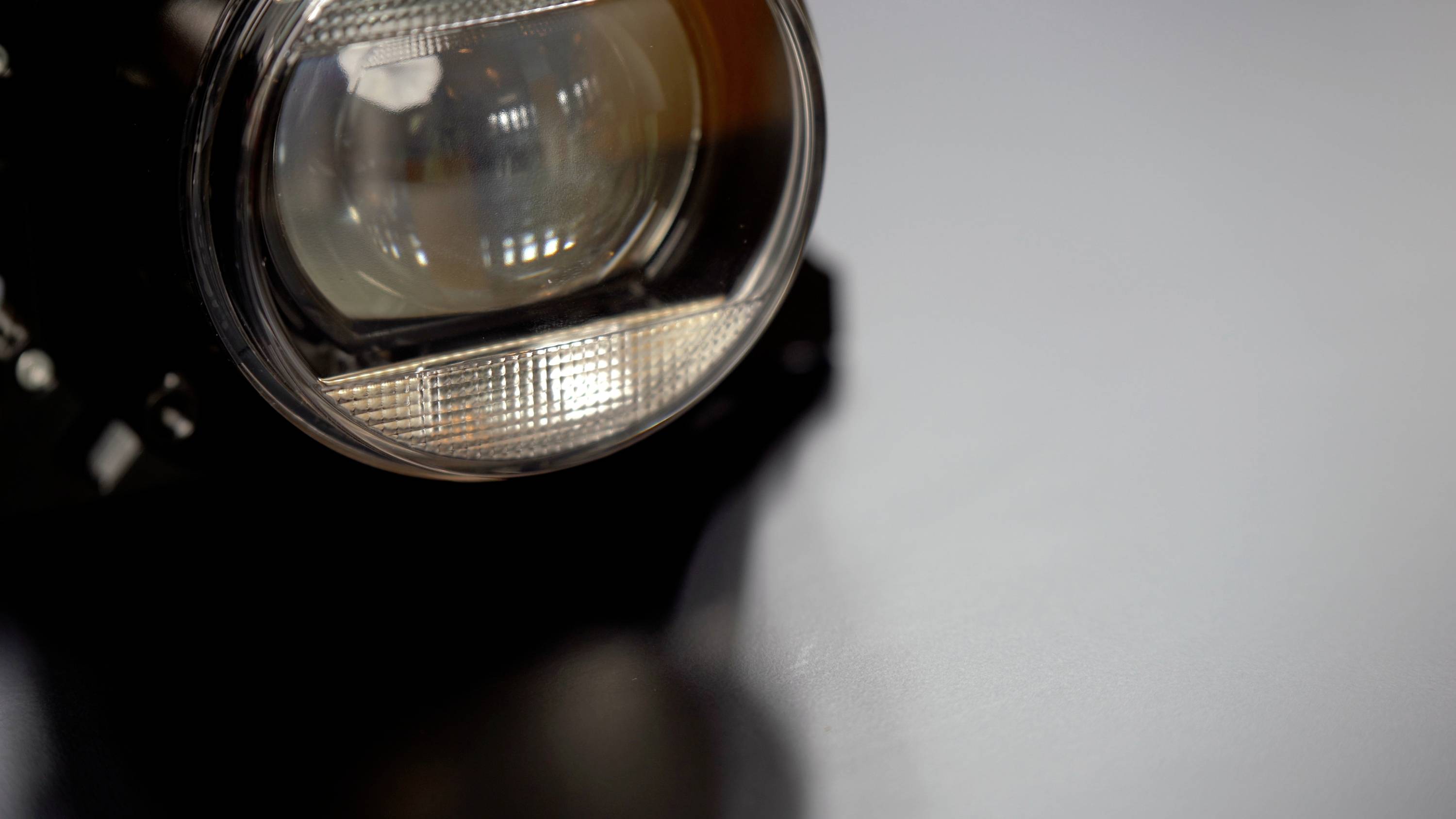 Ein runder Scheinwerfer auf einer glatten, grauen Oberfläche. Reflektionen auf der Linse erzeugen Lichteffekte.