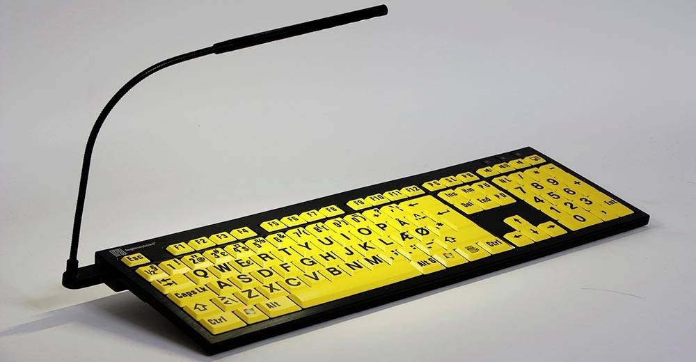 Gelbe Tastatur mit großen, schwarzen Buchstaben und Zahlen, die in Braille und Klartext dargestellt sind, mit Leselampe.